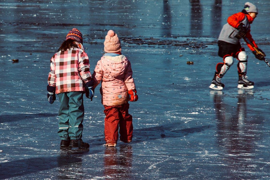 The photograph shows three children skating on ice, one wearing hockey gear.