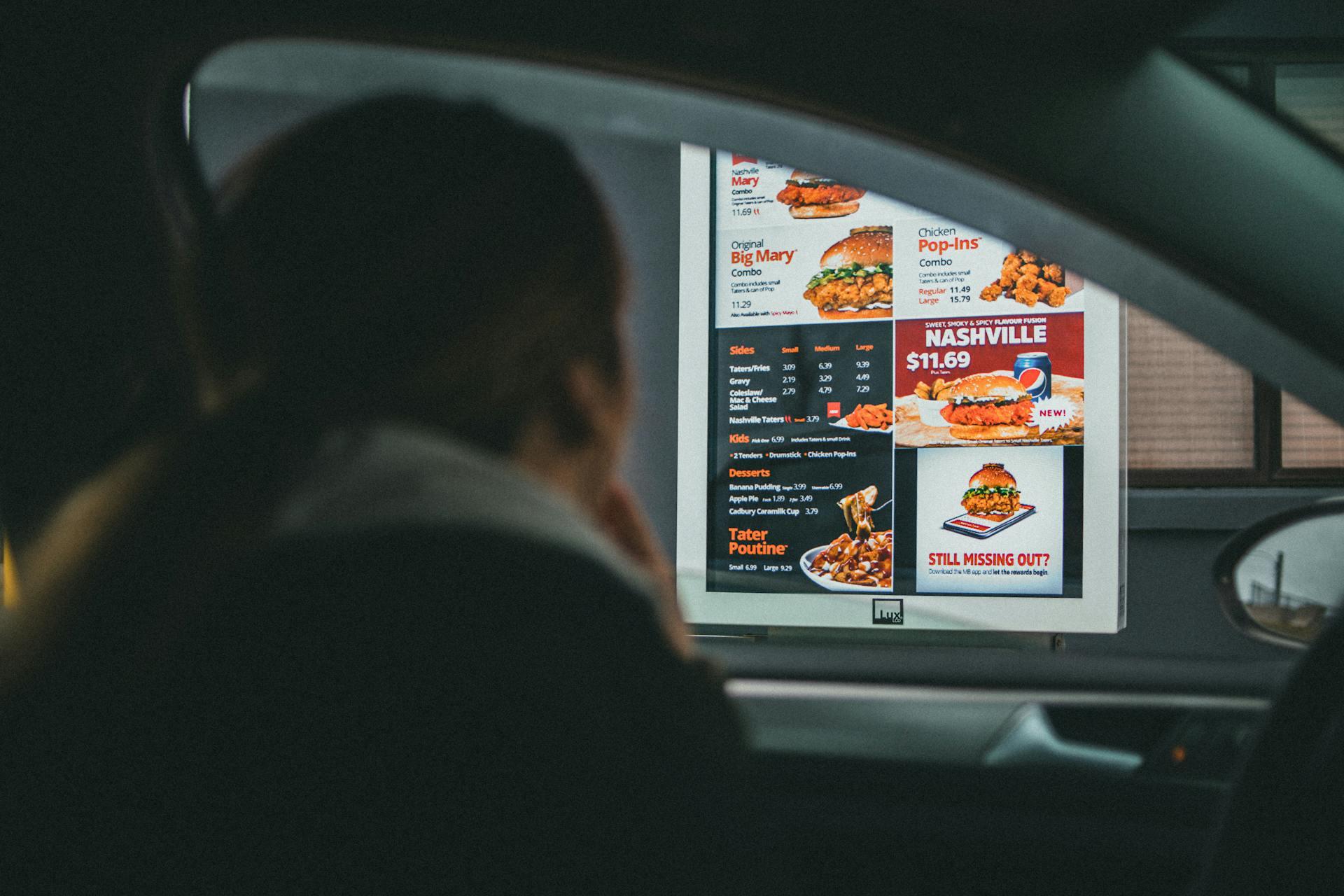 A Woman Sitting Inside the Car Ordering Food. Poutine is visible on the menu.