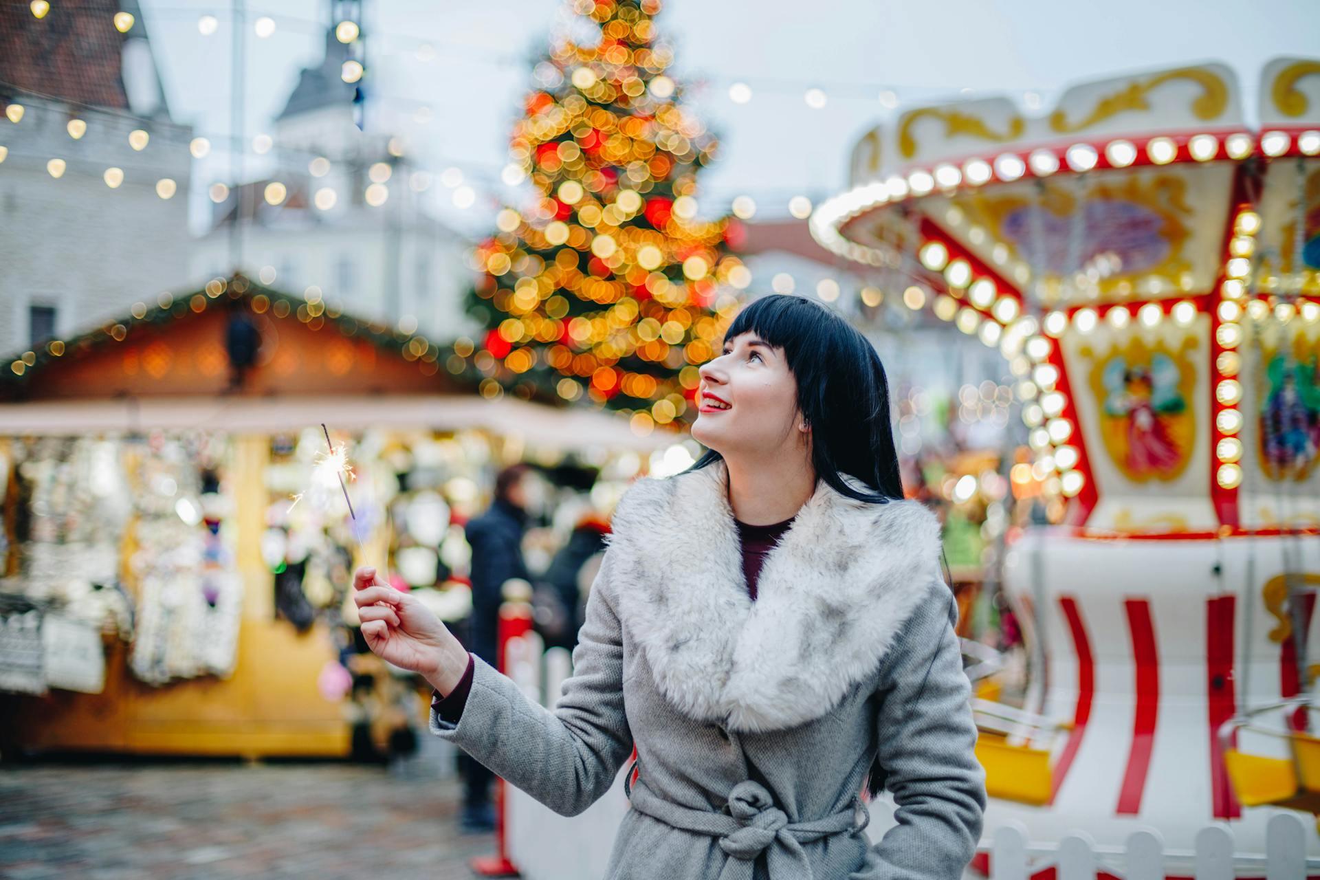 The photograph shows a woman holding a sparkler at a Christmas fair.