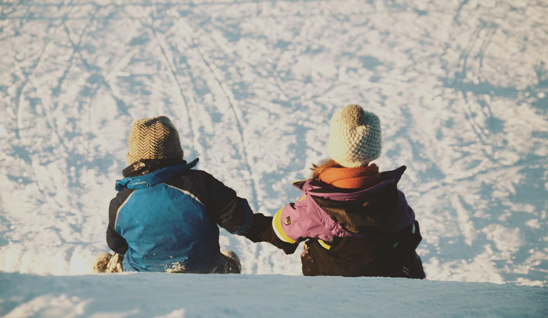 two kids sitting in the snow holding hands