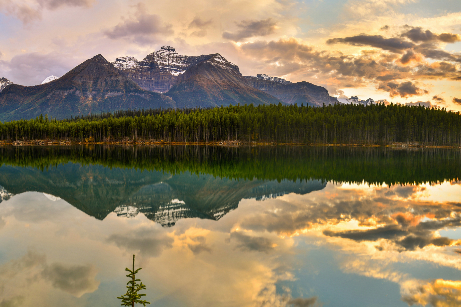 A vibrant sunset reflecting off the calm waters of a lake with towering mountains in Banff National Park.
