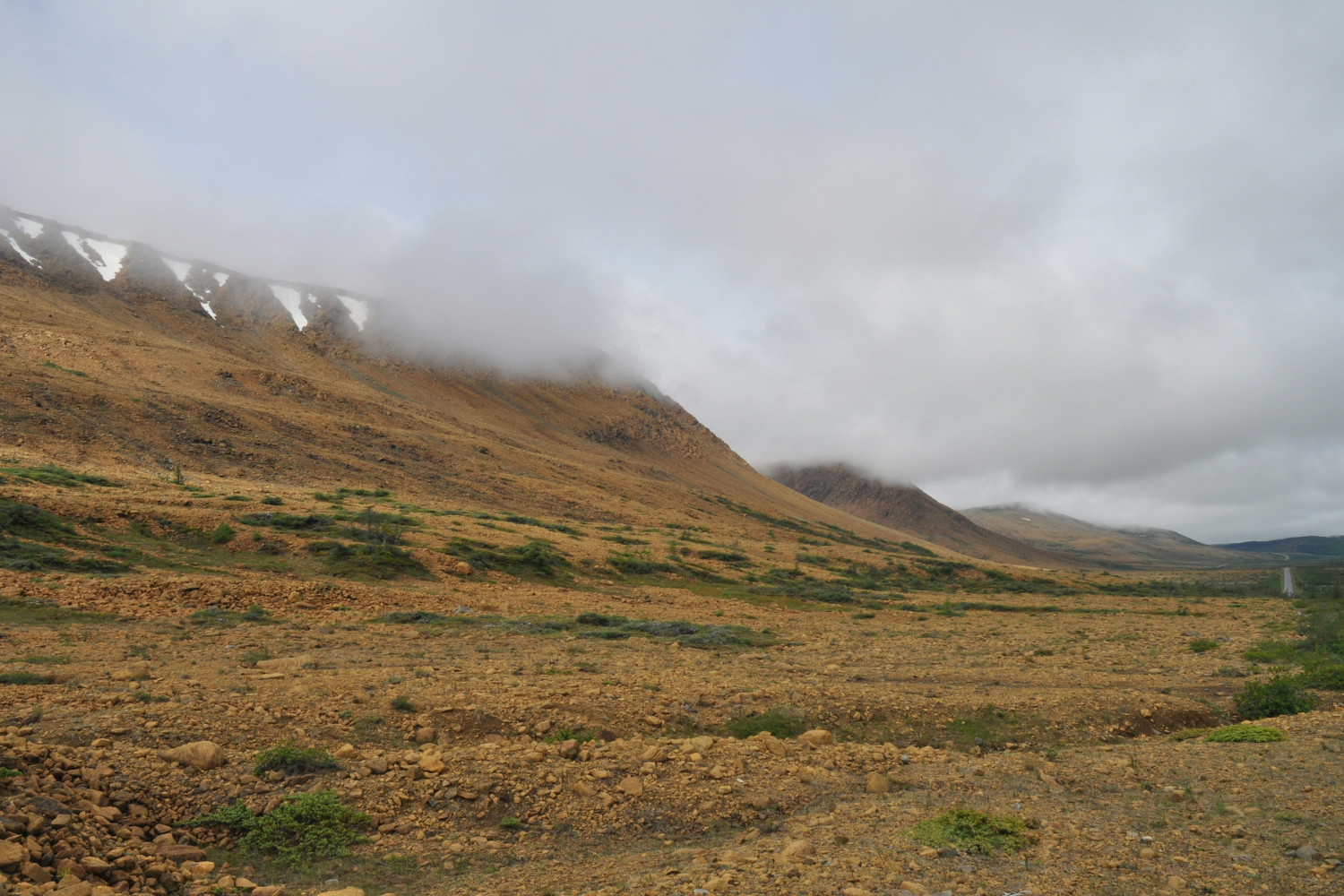 The barren, rocky landscape of the Tablelands in Gros Morne National Park, with clouds hanging low over the mountain ridges.
