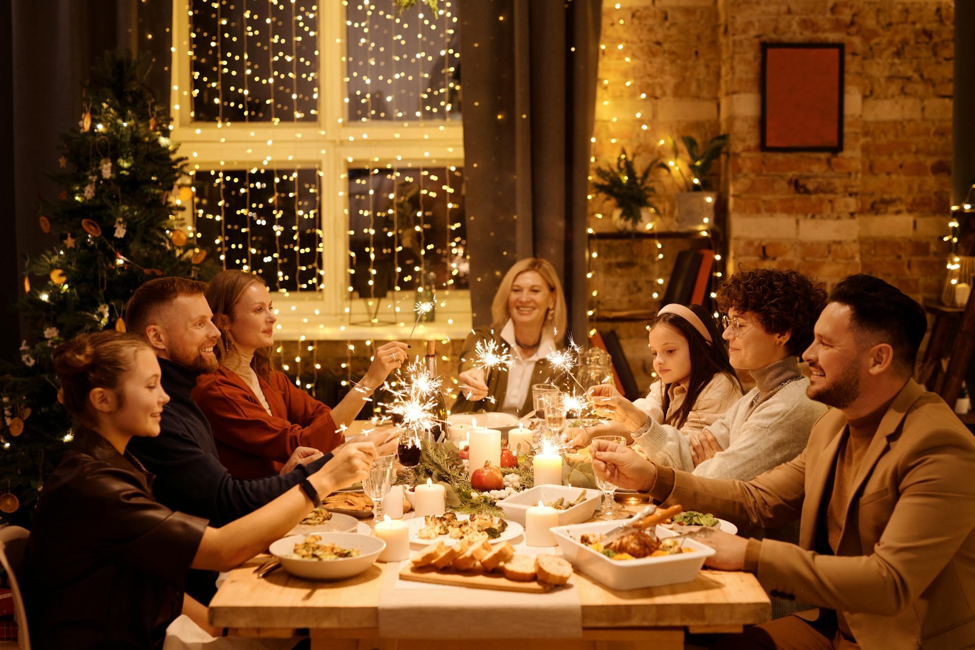 The photograph shows a Christmas dinner where we see several people sitting around a table eating and celebrating.
