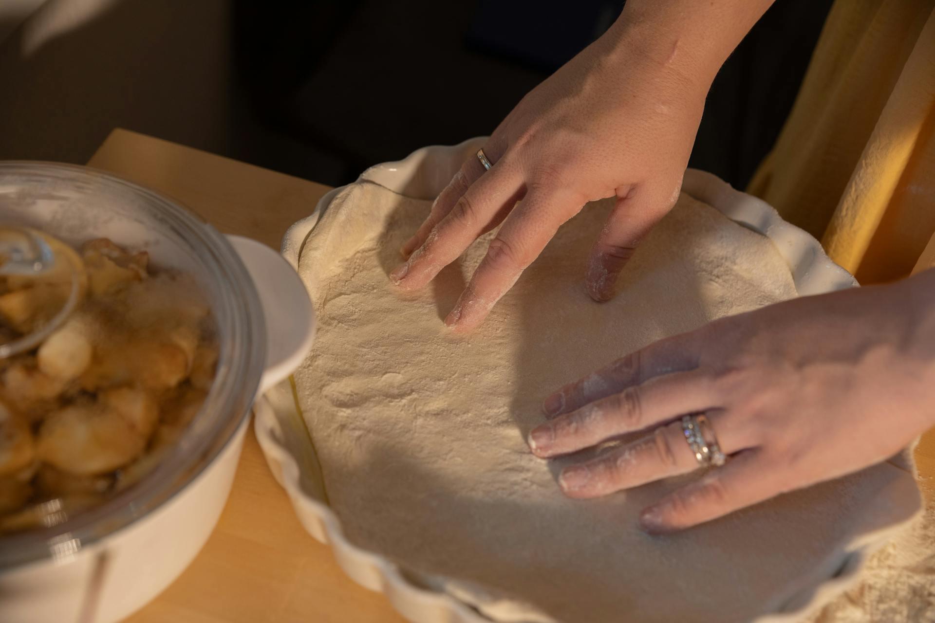 The photograph shows the hands of a person kneading dough with his hands on a wooden table.