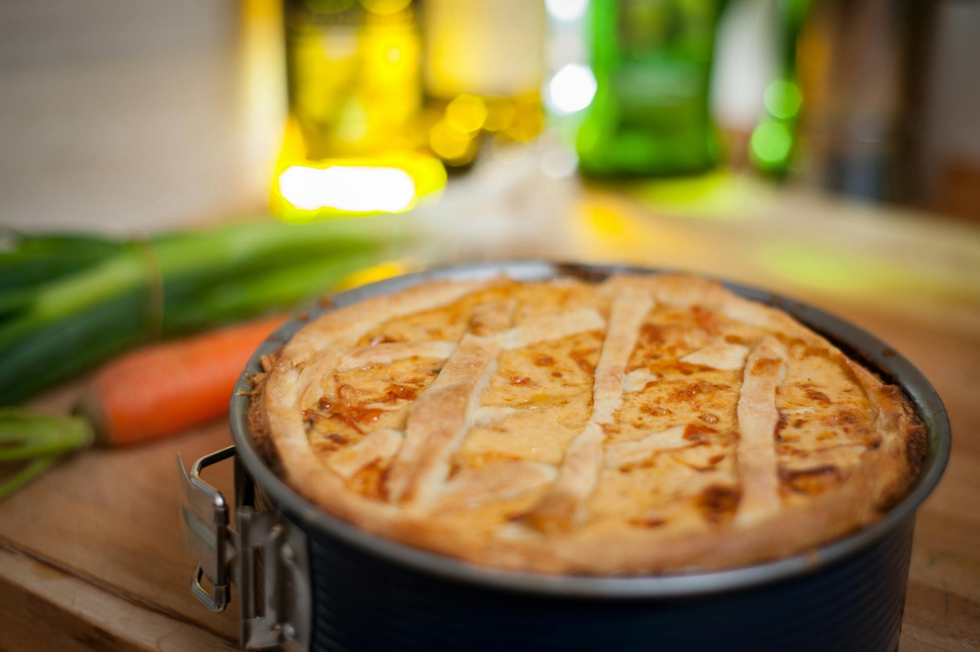 The photograph shows a baked tourtiere cake and in the background is the image of a kitchen.