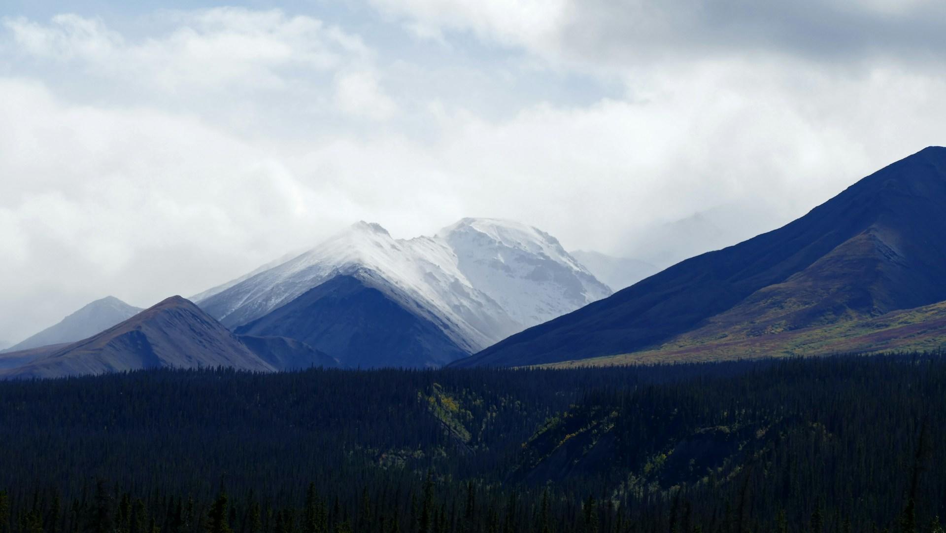 Snow-capped mountains touching the overcast sky - wild terrain of Yukon.