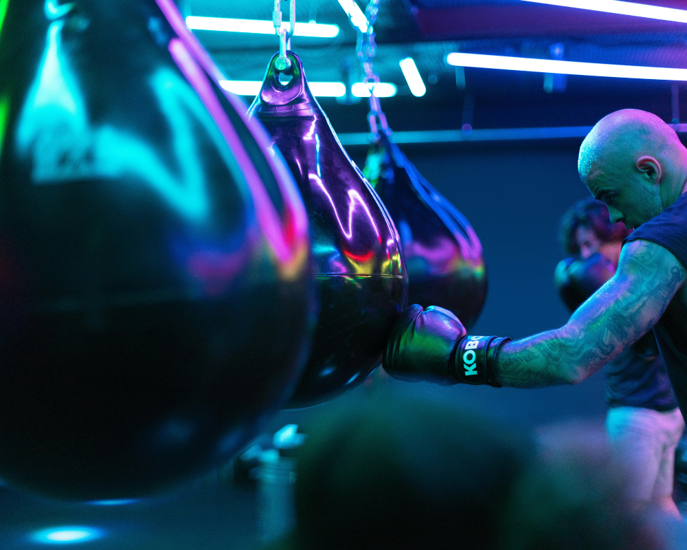 Person training with boxing gloves in a gym with neon lighting in Montreal, hitting a heavy bag.