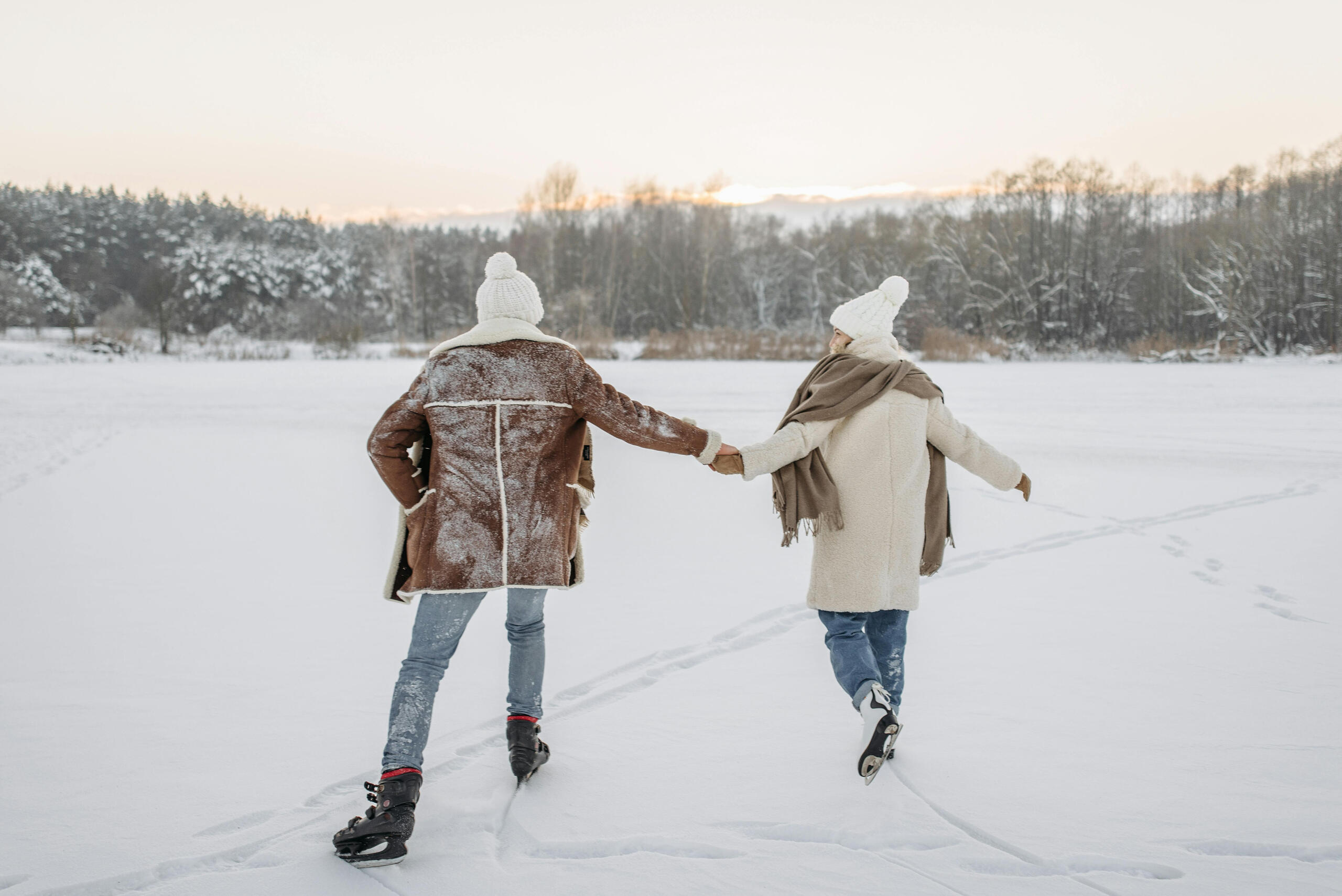 a man and woman skate on a snowy pond. 