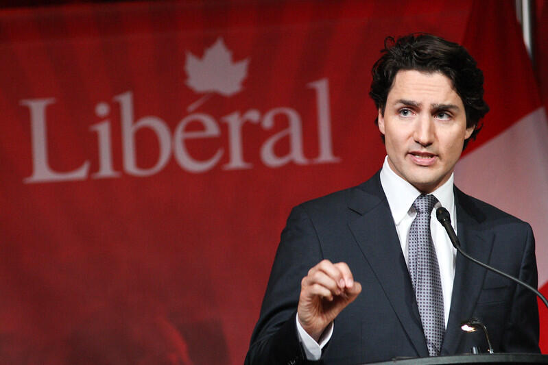Justin Trudeau giving a speech with his party's logo as a backdrop.