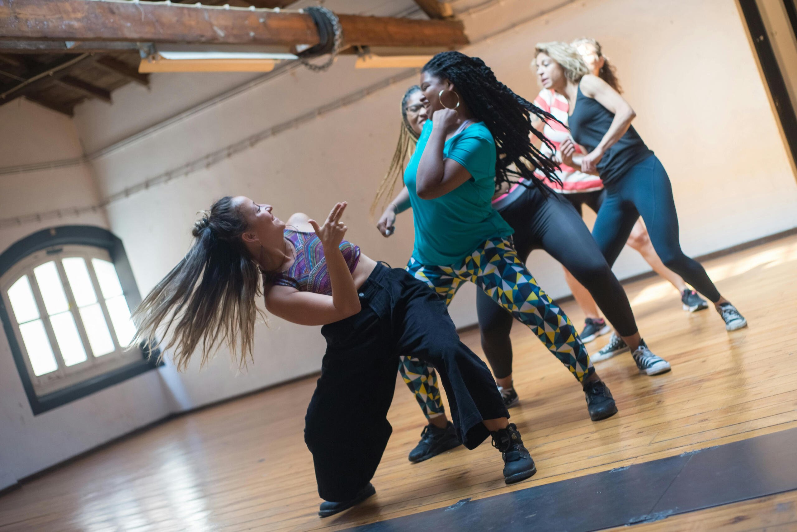 A group of people participating in a high-energy dance fitness class, with various individuals performing dance moves in a studio setting.