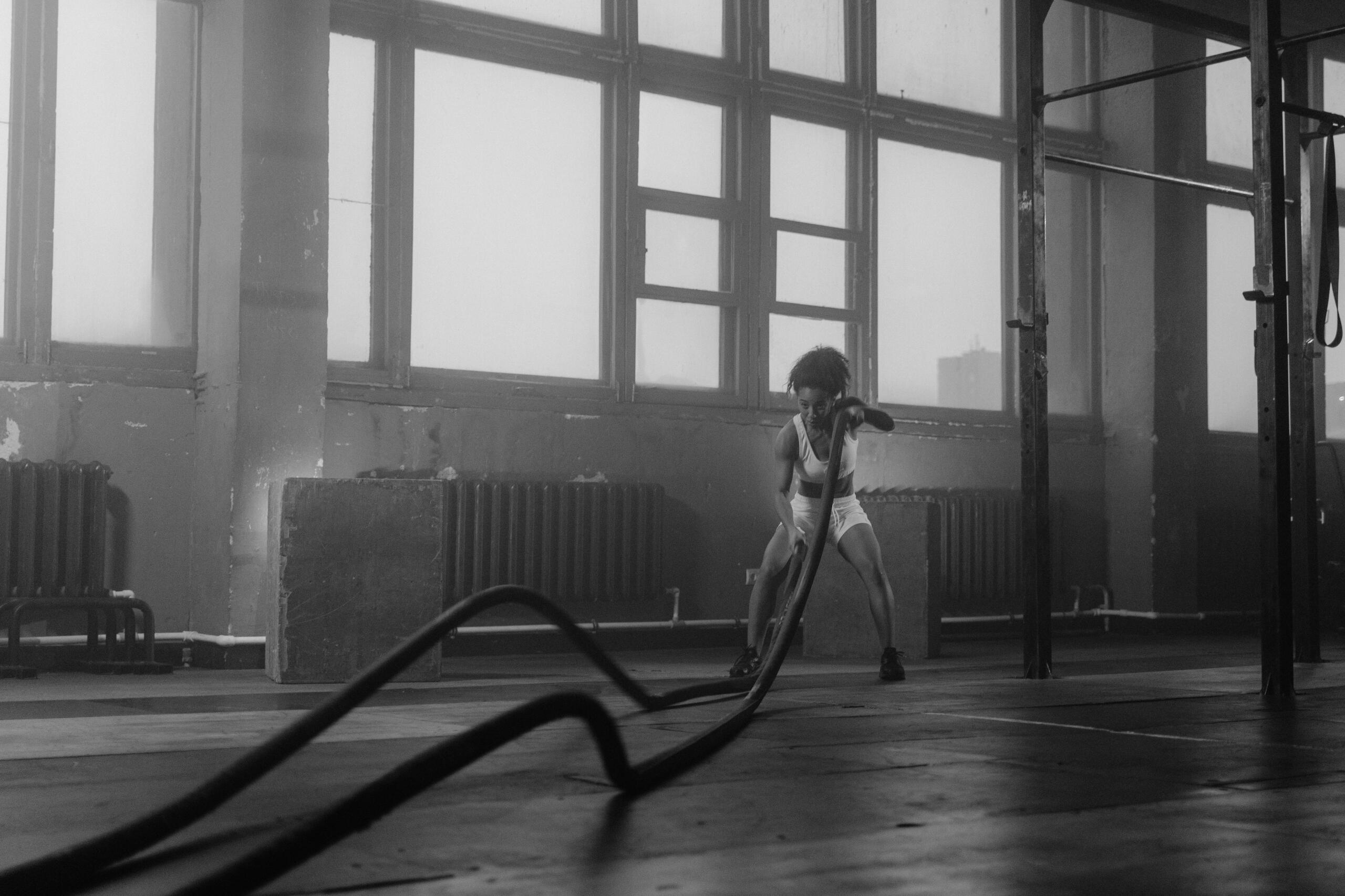 A person engaging in battle rope exercises in an industrial-style gym, working on building strength and endurance.