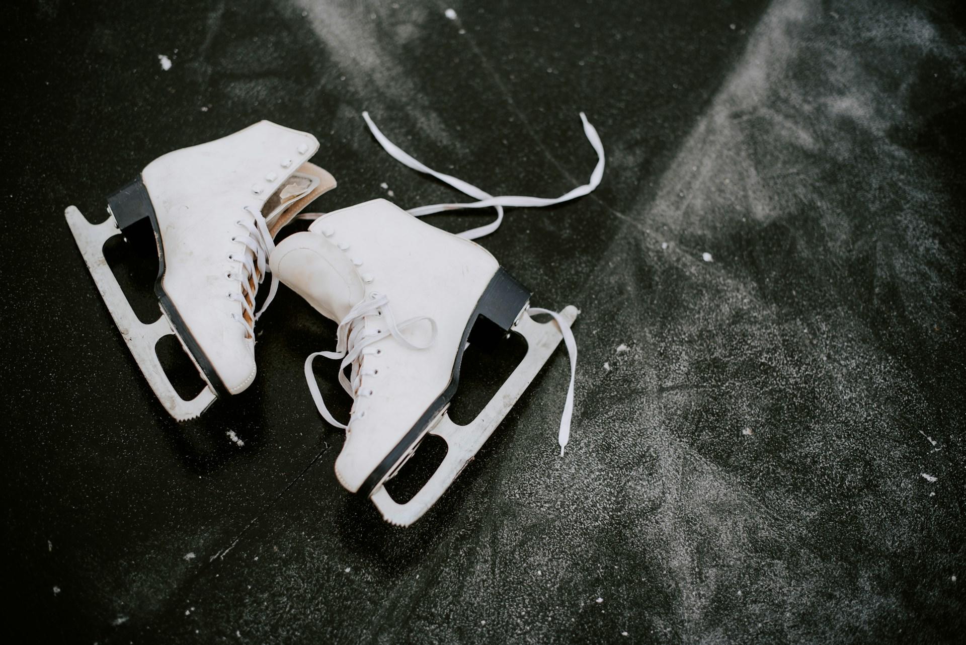 A pair of white ice skates on a dark frozen surface.