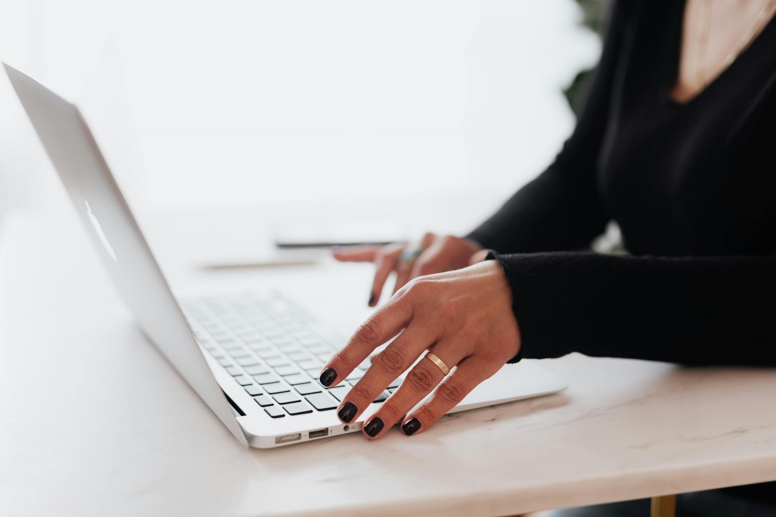 a woman wearing a wedding ring works on a laptop. Her face is not shown.
