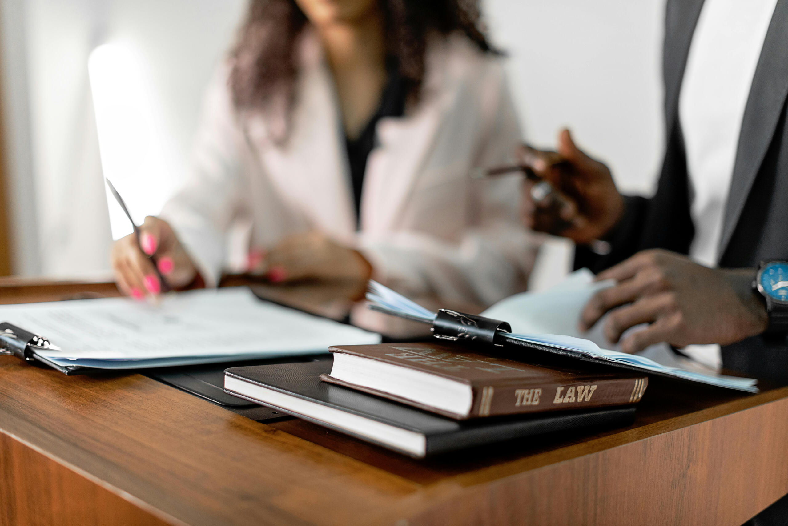 a male and female lawyer look at clipboards and law books at a desk.