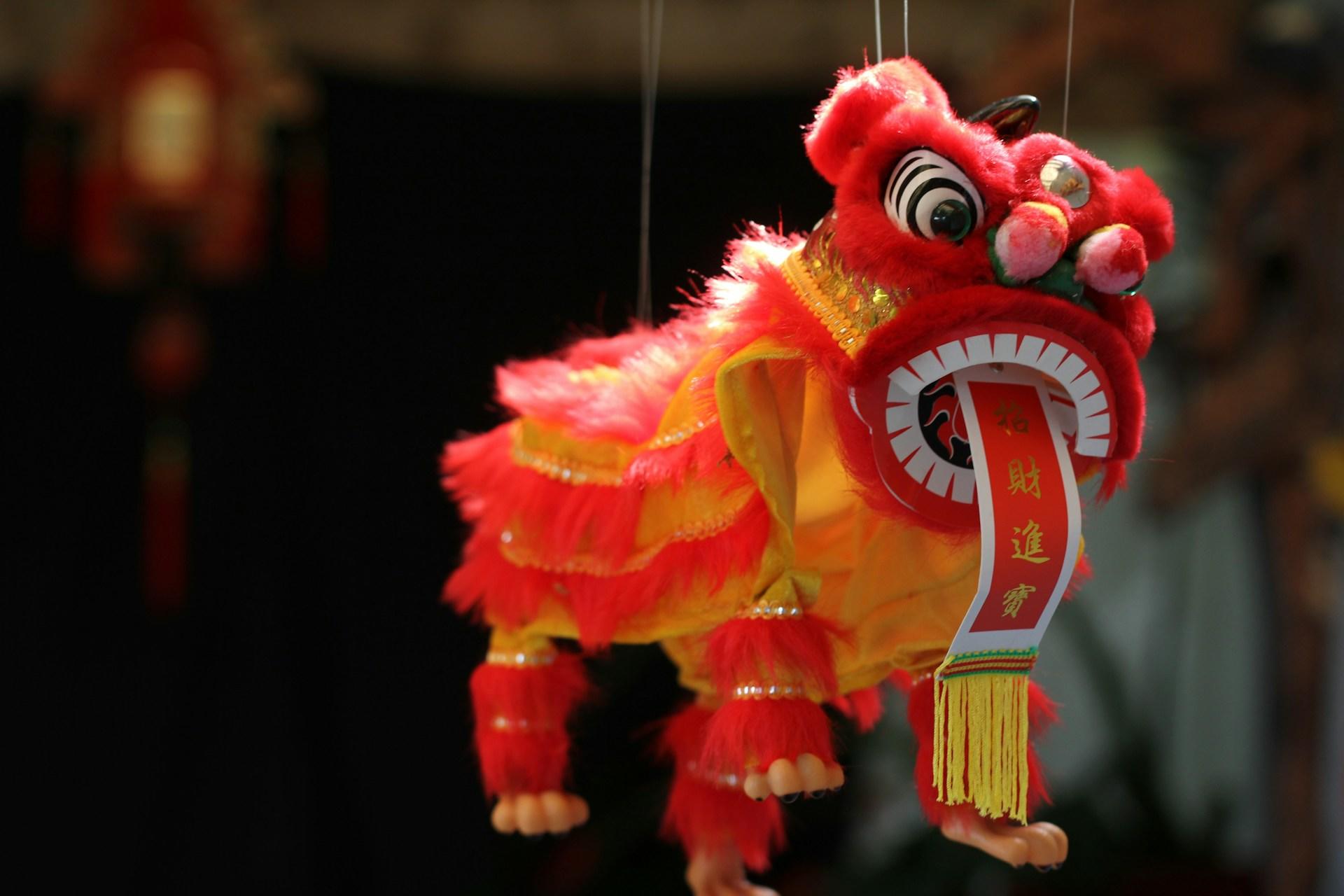 A red and yellow traditional Chinese lion dance puppet with a festive ribbon hanging underneath.