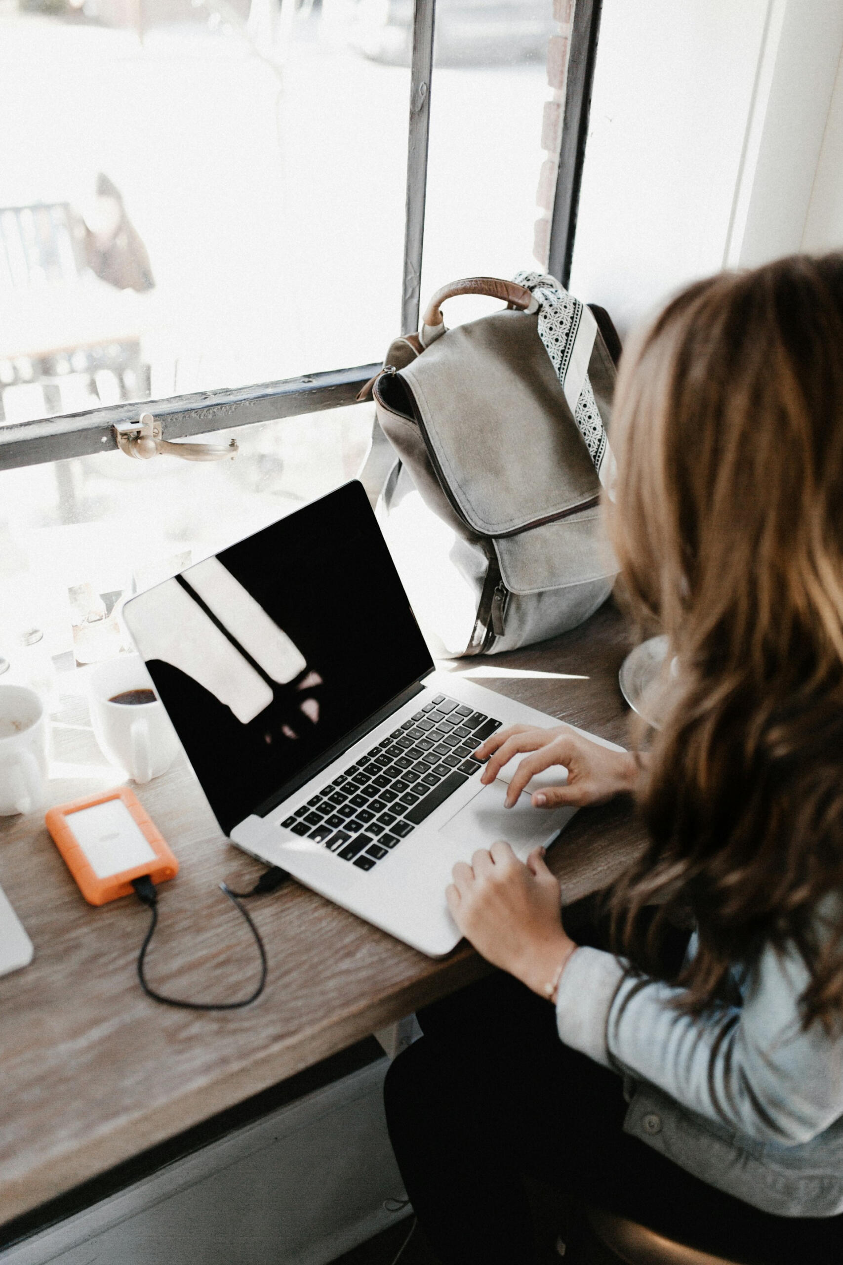 A female typing something on her laptop with her bag on a table. 