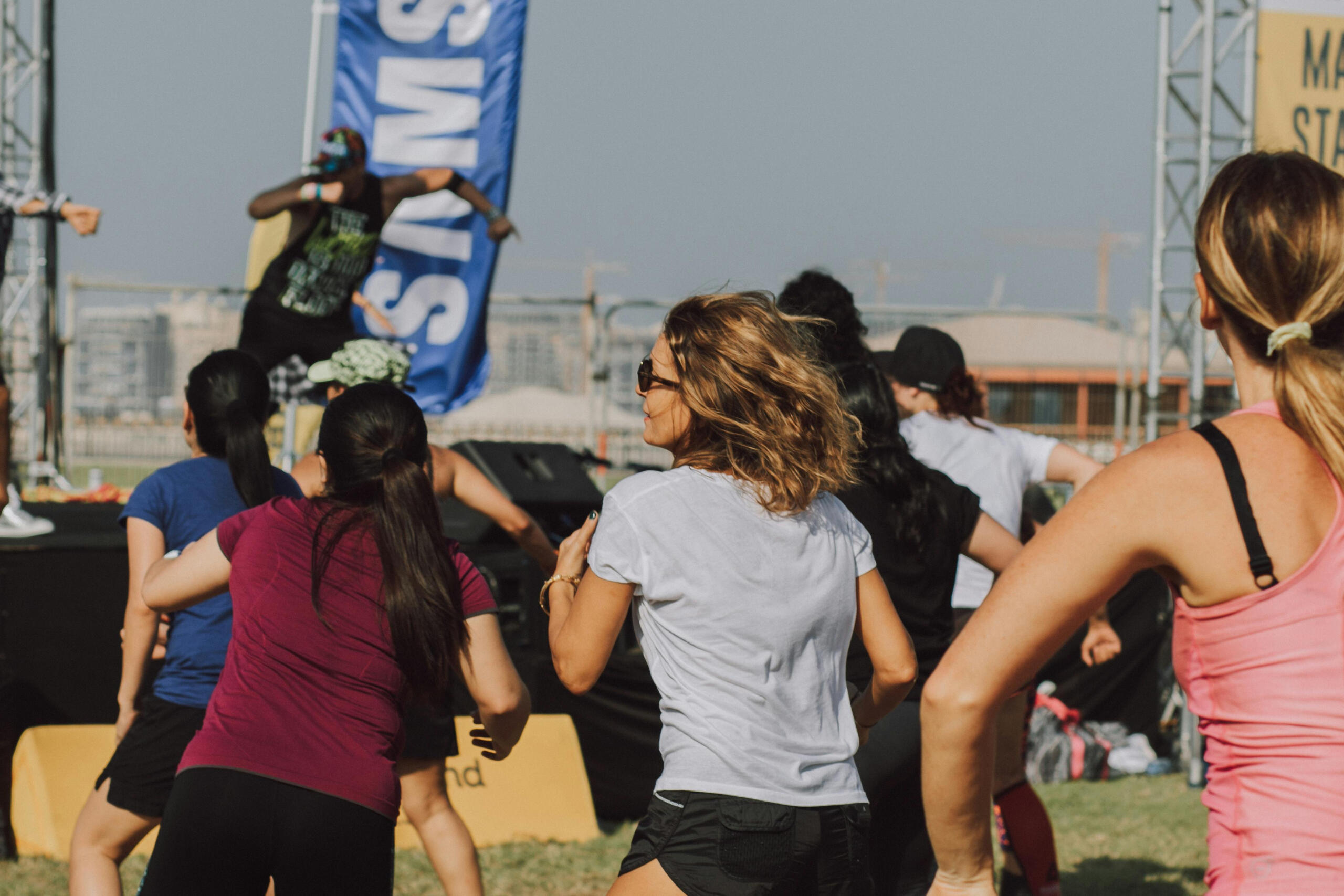 A group of people participating in an outdoor Zumba class, dancing in the sunshine.