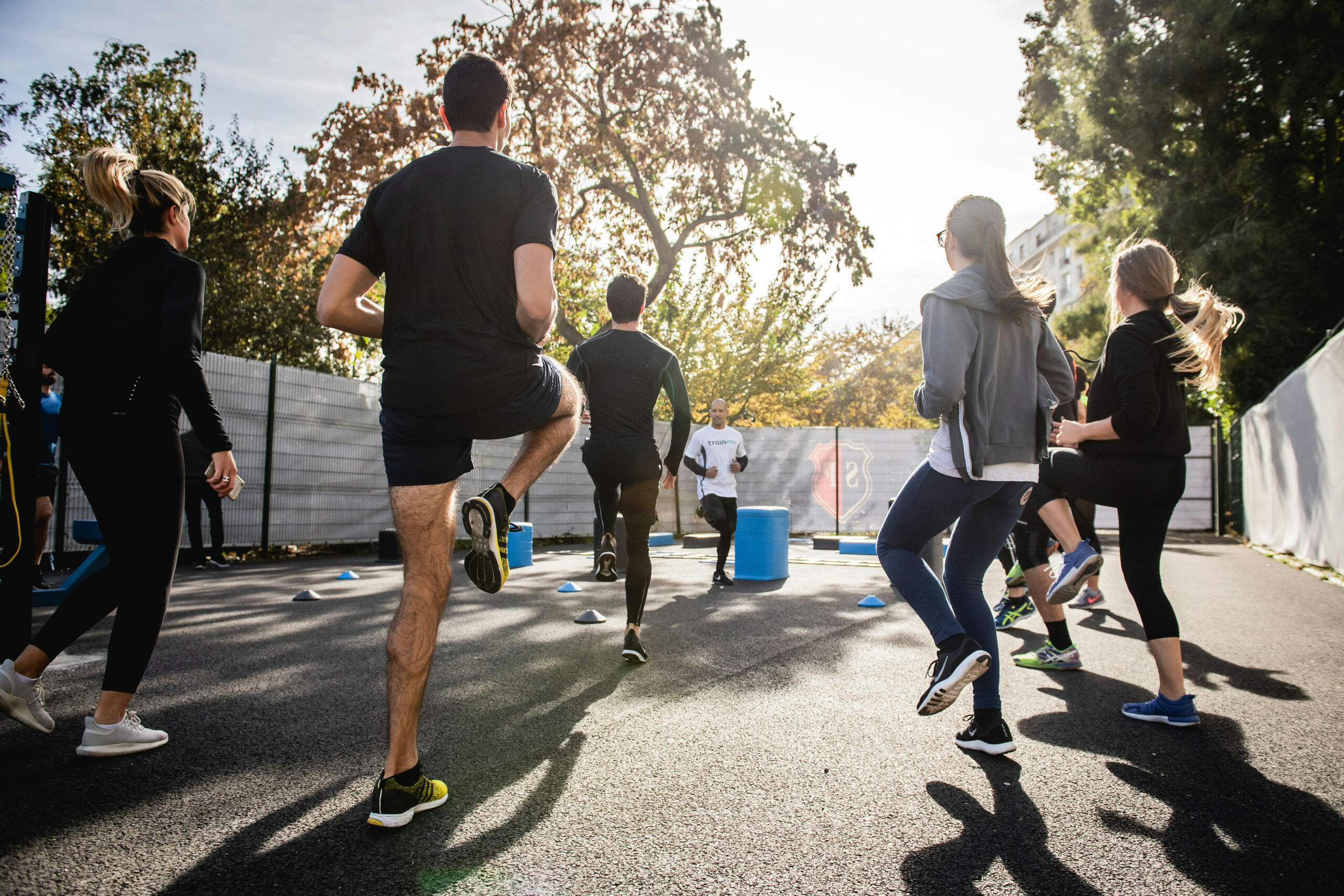 A group of individuals participating in an outdoor fitness class, performing high knees while running in a sunny park setting.