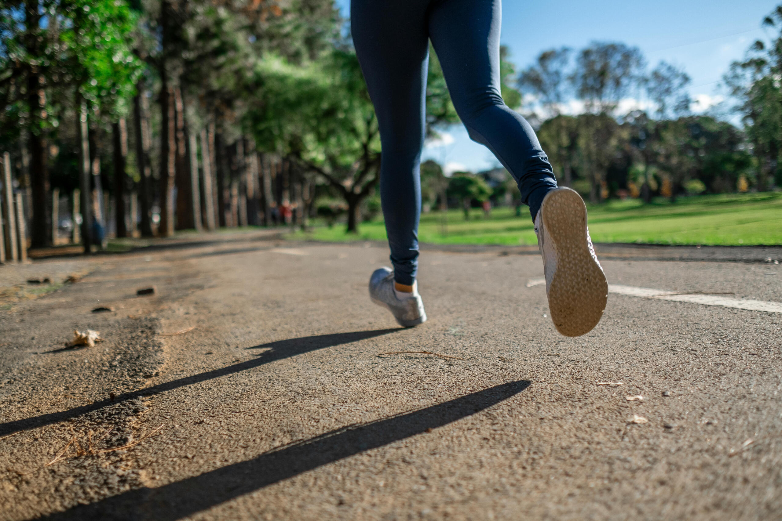 A person in fitted pants runs on a path near a forest.