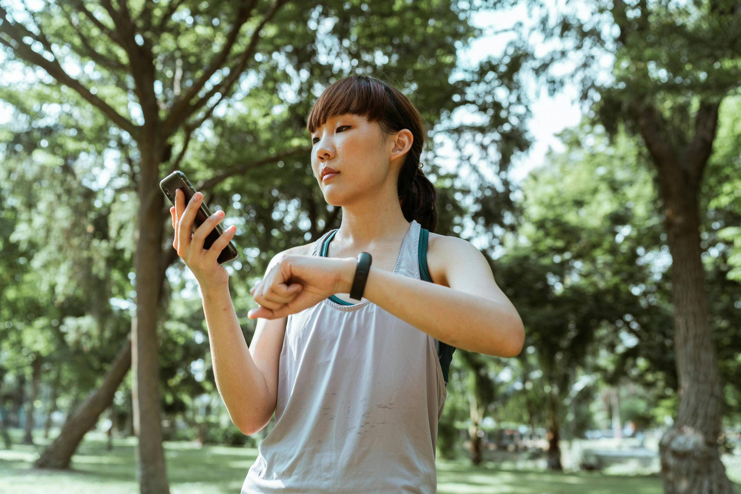 A woman looks at a smartphone as it synchronizes with her fitness watch. Trees are in the background.