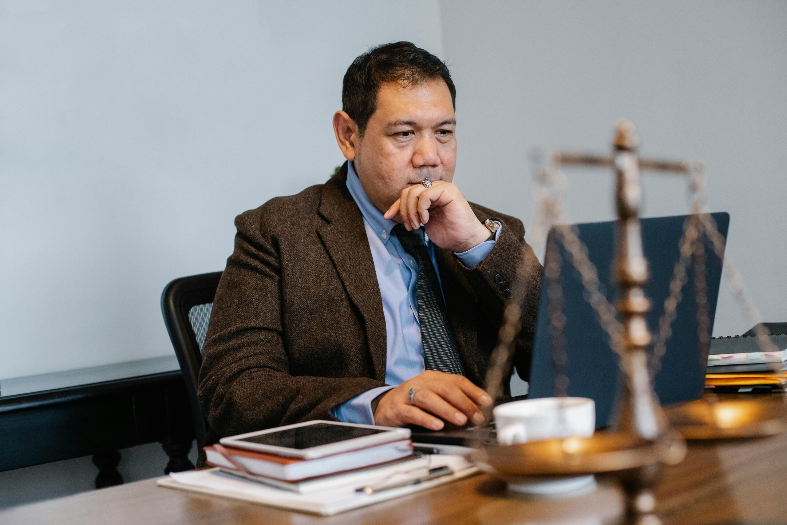 A male lawyer sits in front of a computer. The scales of justice can be seen on his desk.