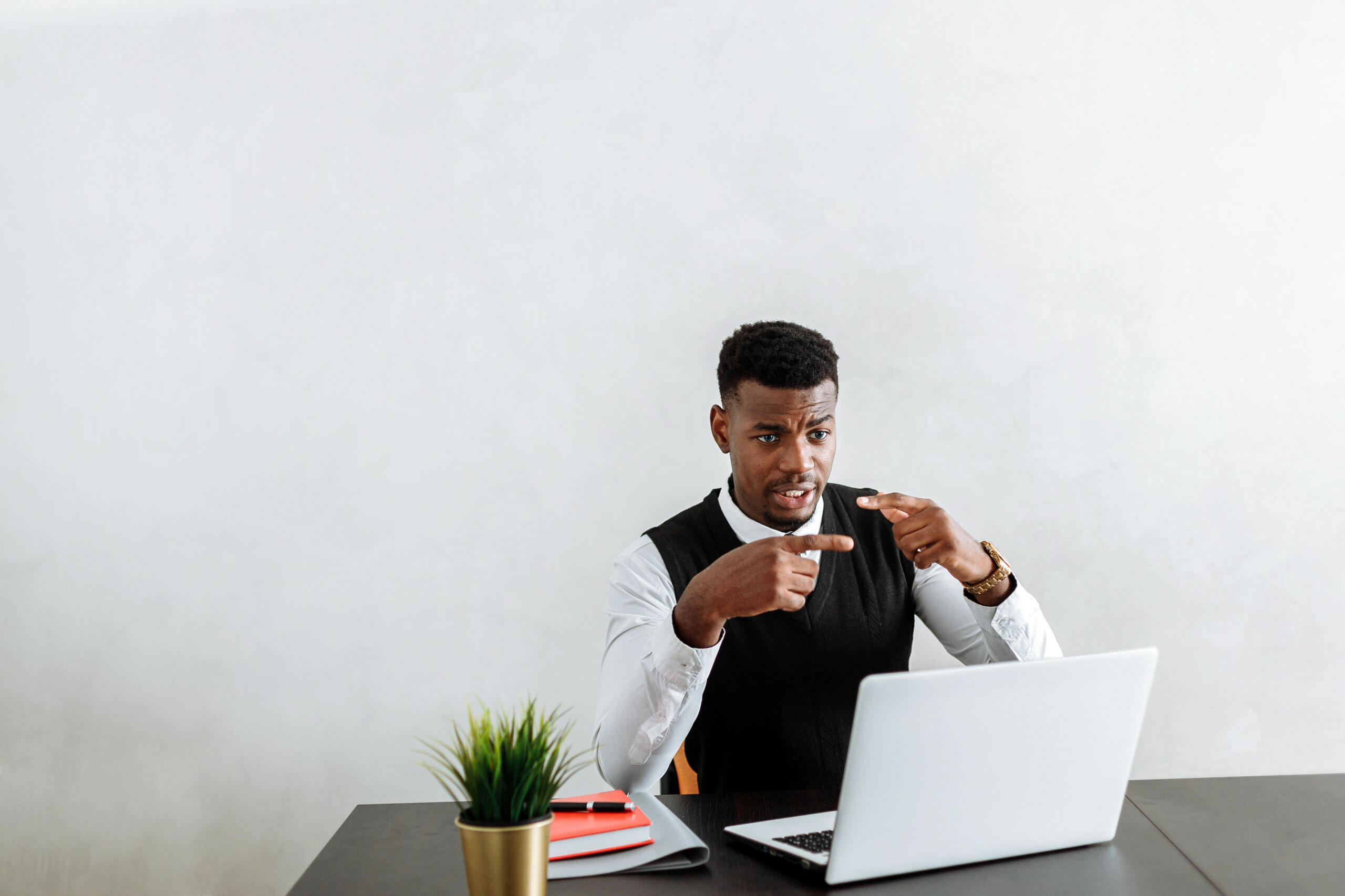 a man looks at a computer on a desk. The wall behind him is blank.