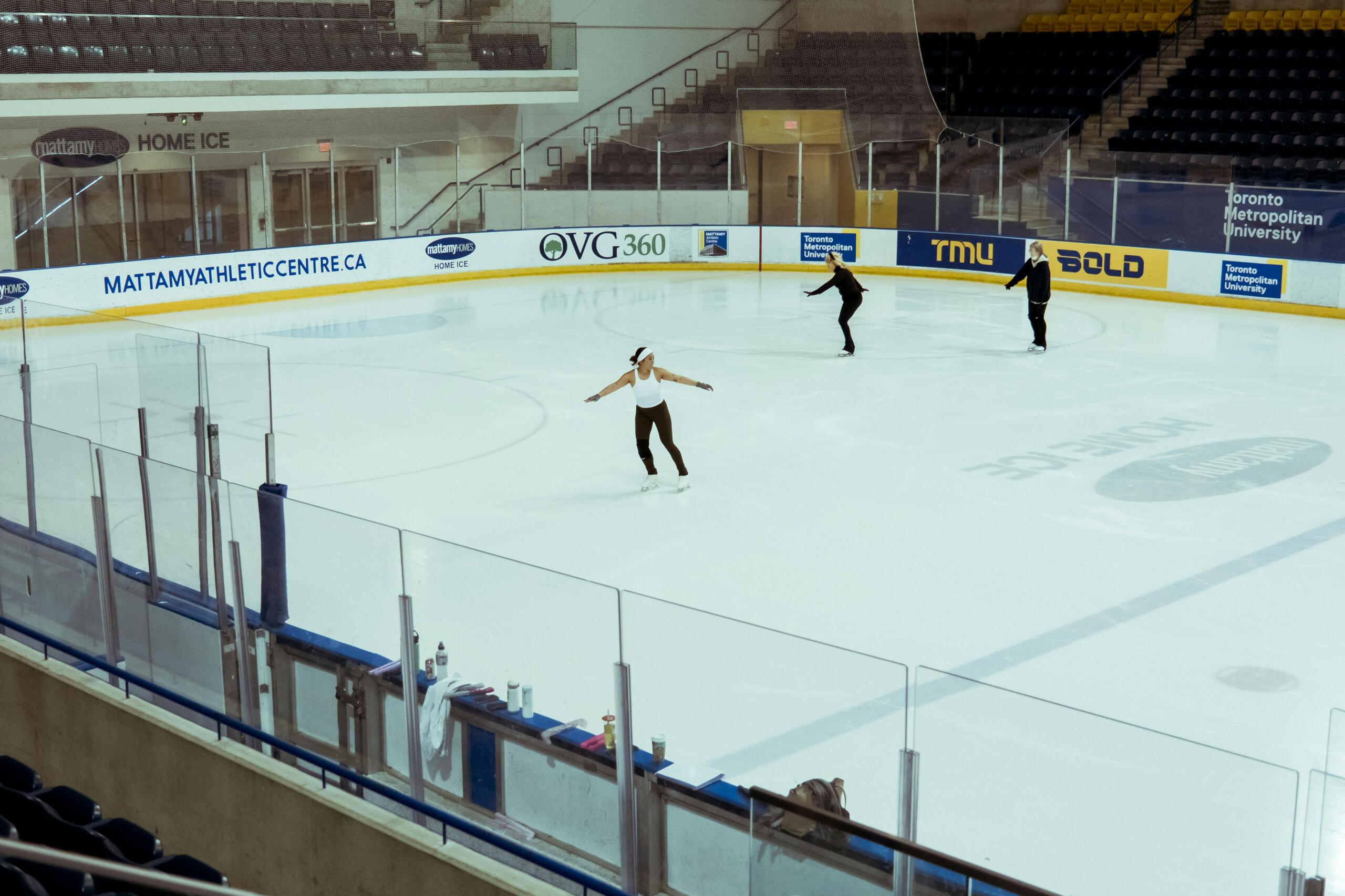 Multiple figure skaters practice in an indoor rink.