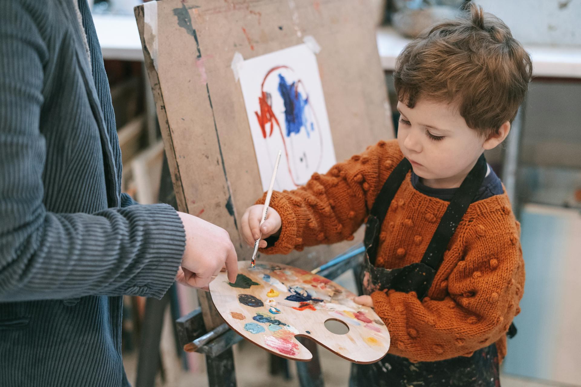 Boy in orange and black zip up Jacket holding white and red floral round plate.
