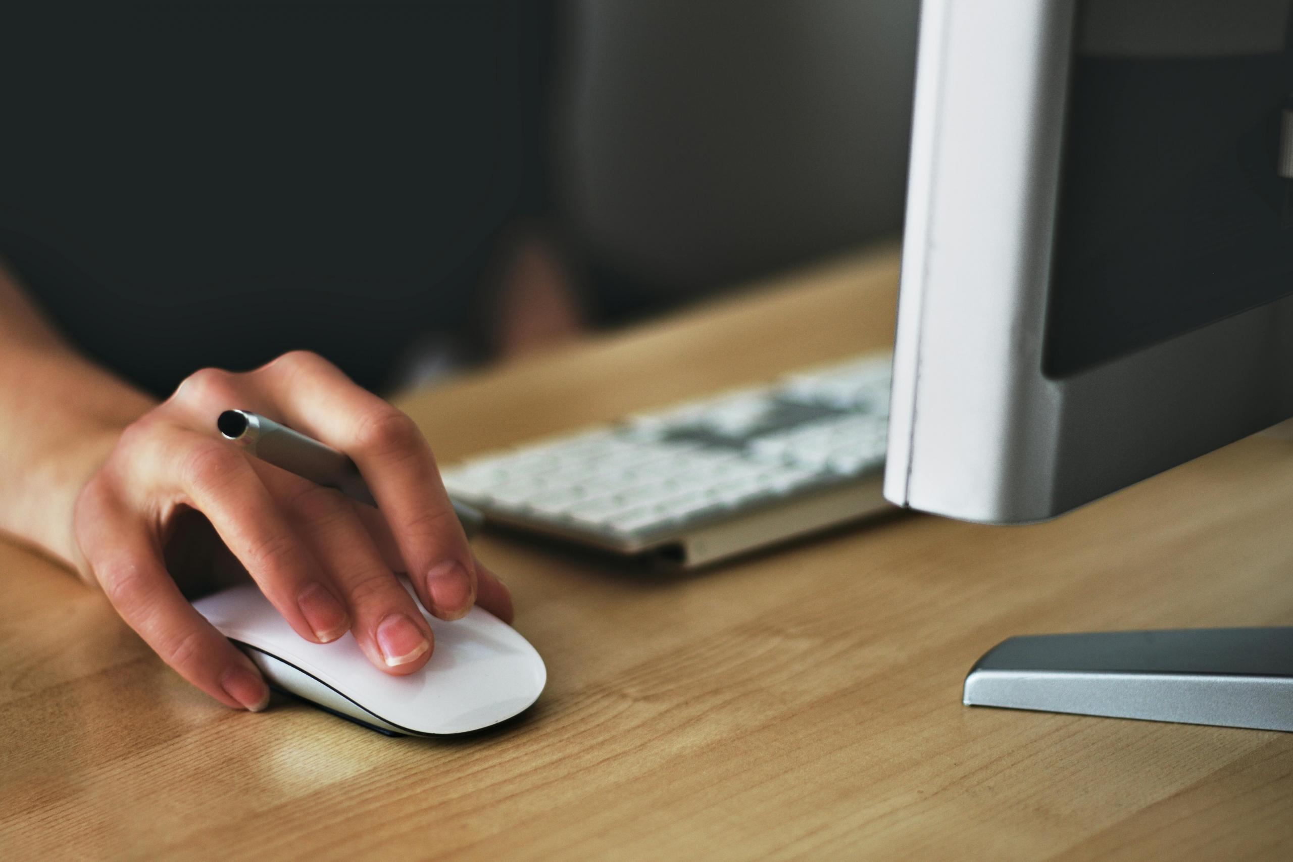 a woman's hand can be seen moving a mouse. A desktop computer is on a desk beside the mouse.