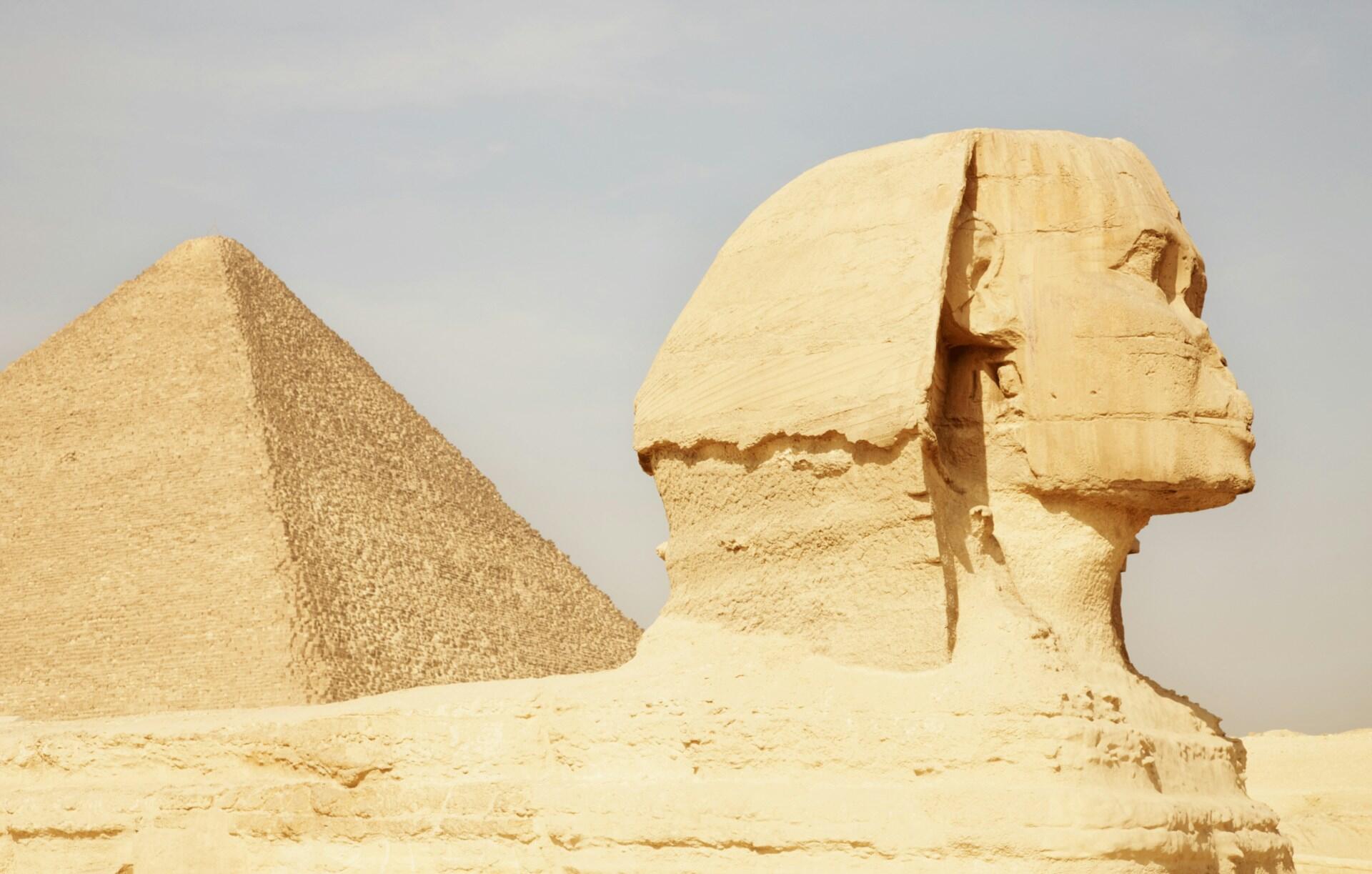 Great Sphinx with a pyramid in the background under a clear sky.
