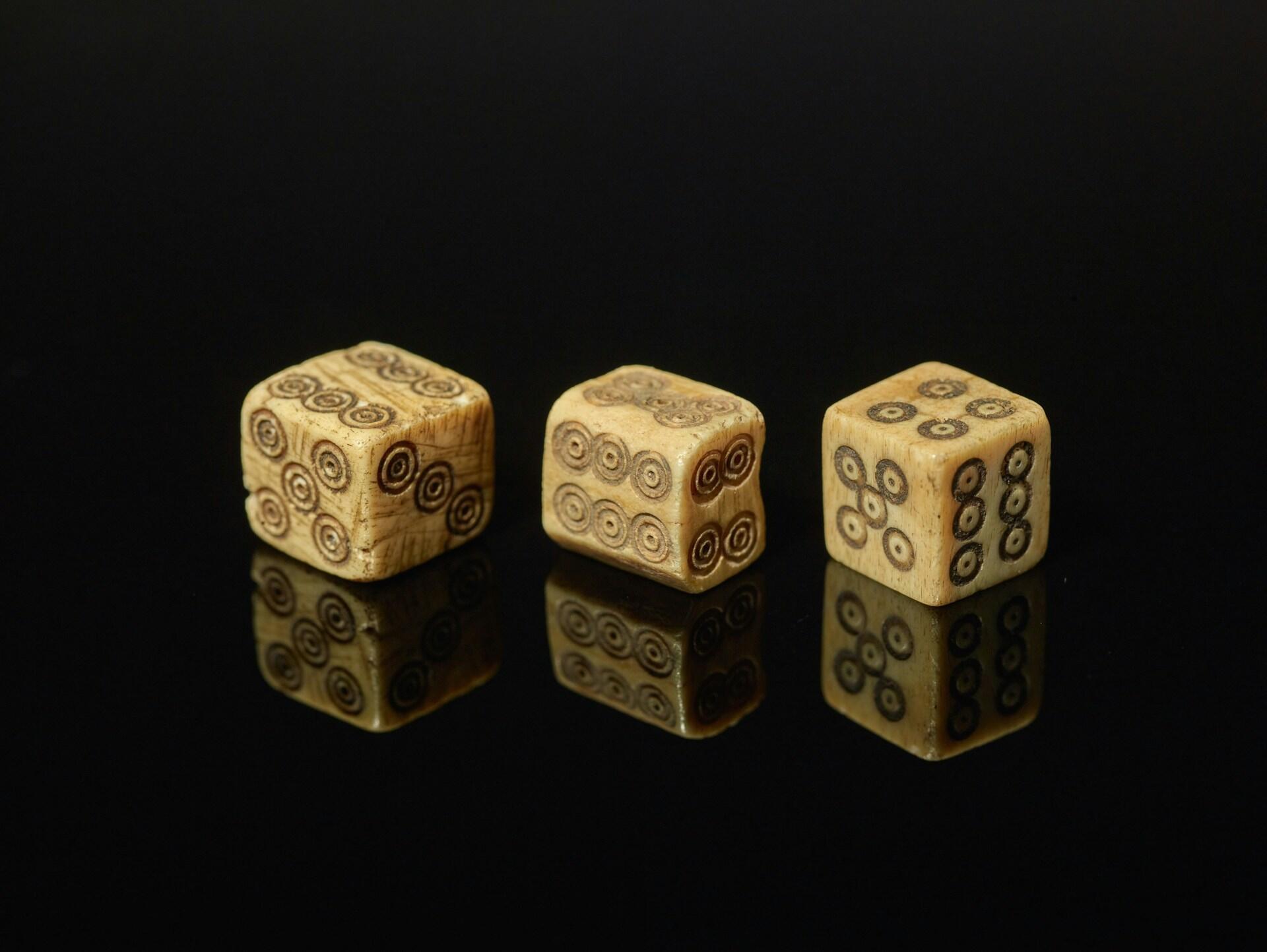Three aged dice with spiral patterns on a reflective black surface.