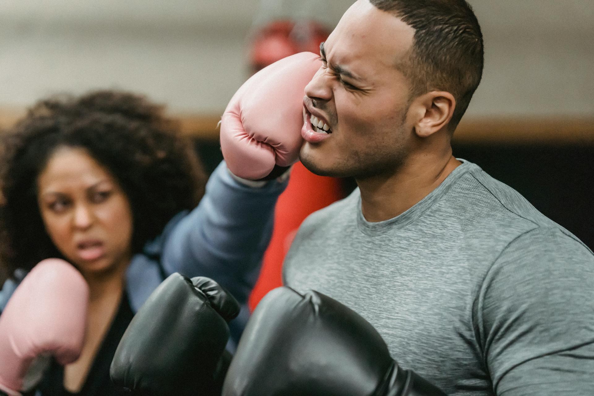 We see two people training during a boxing class, using boxing globes.