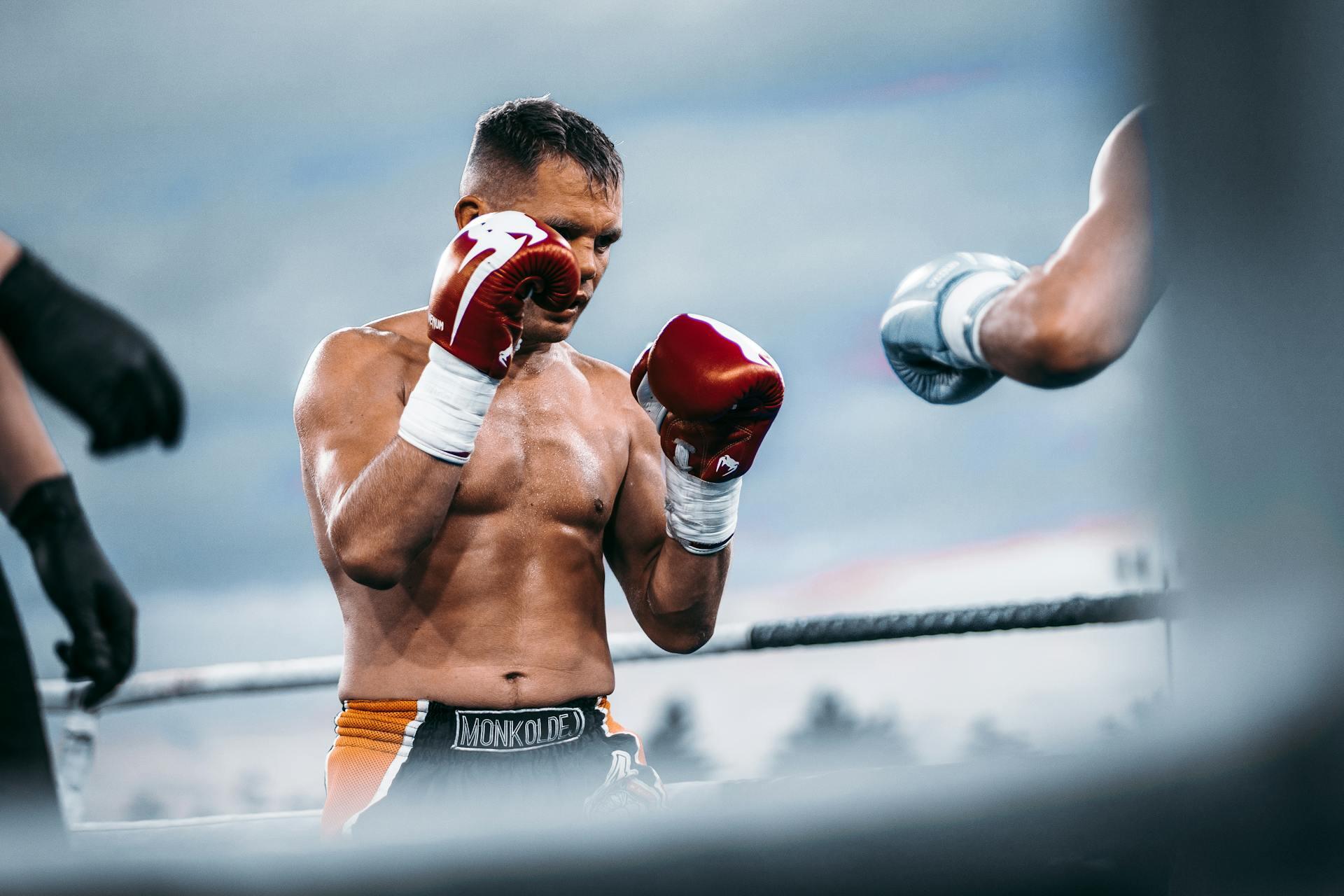 A Man in the ring wearing red boxing gloves, with a glimpse of his opponent at the edge of the image.