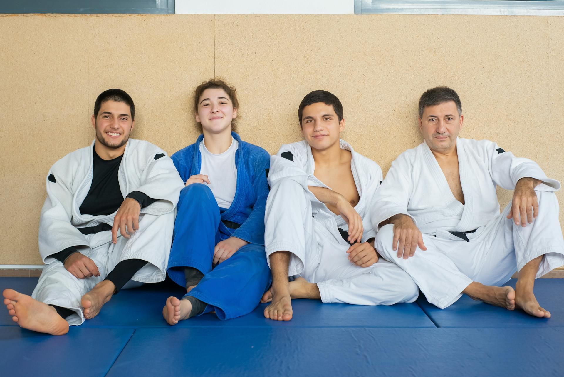 4 martial artists sitting against the wall after a session, wearing their gis and belts.