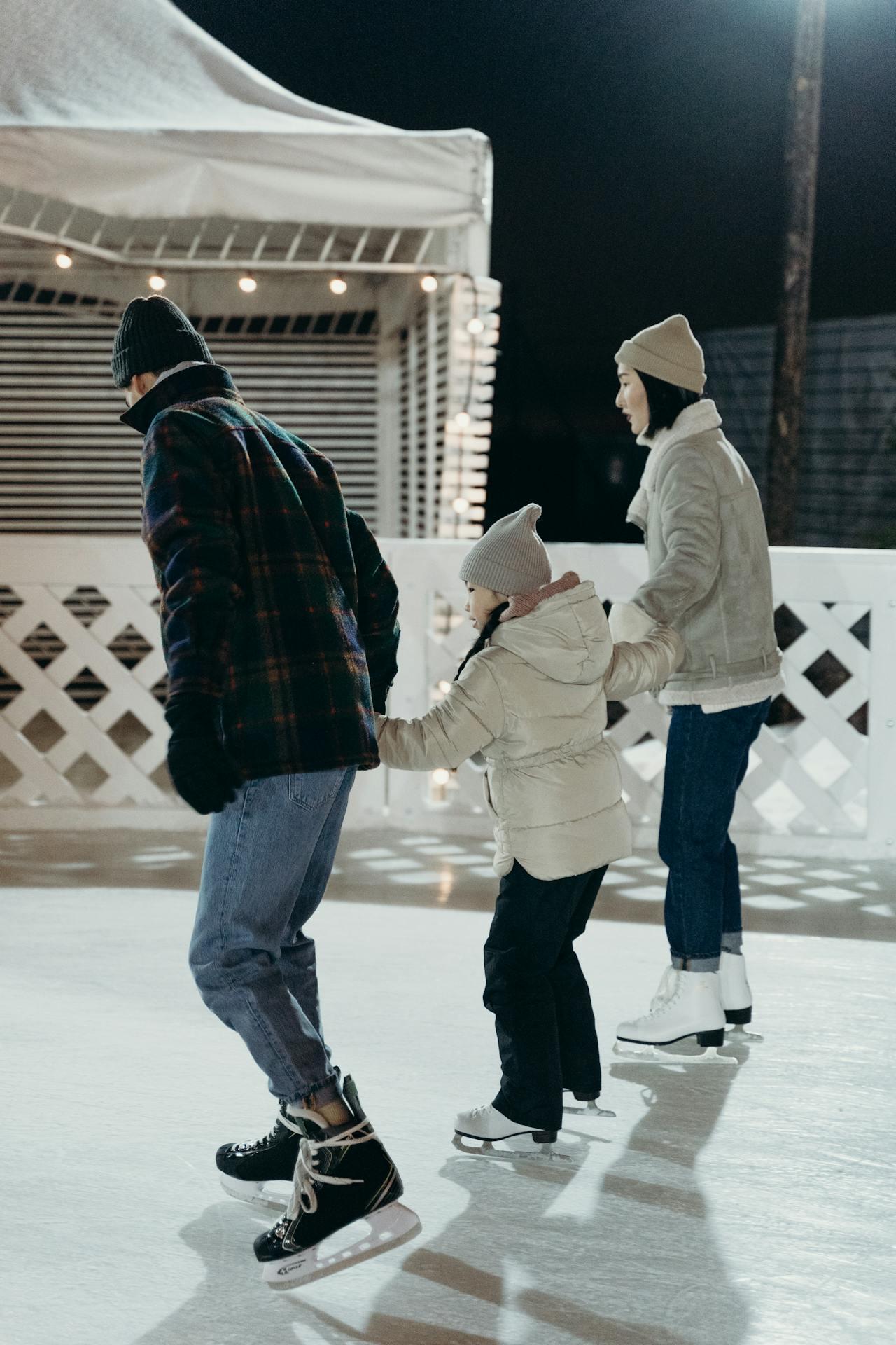 A family enjoys ice skating together at night, with festive lights illuminating the rink and everyone bundled in warm clothing.