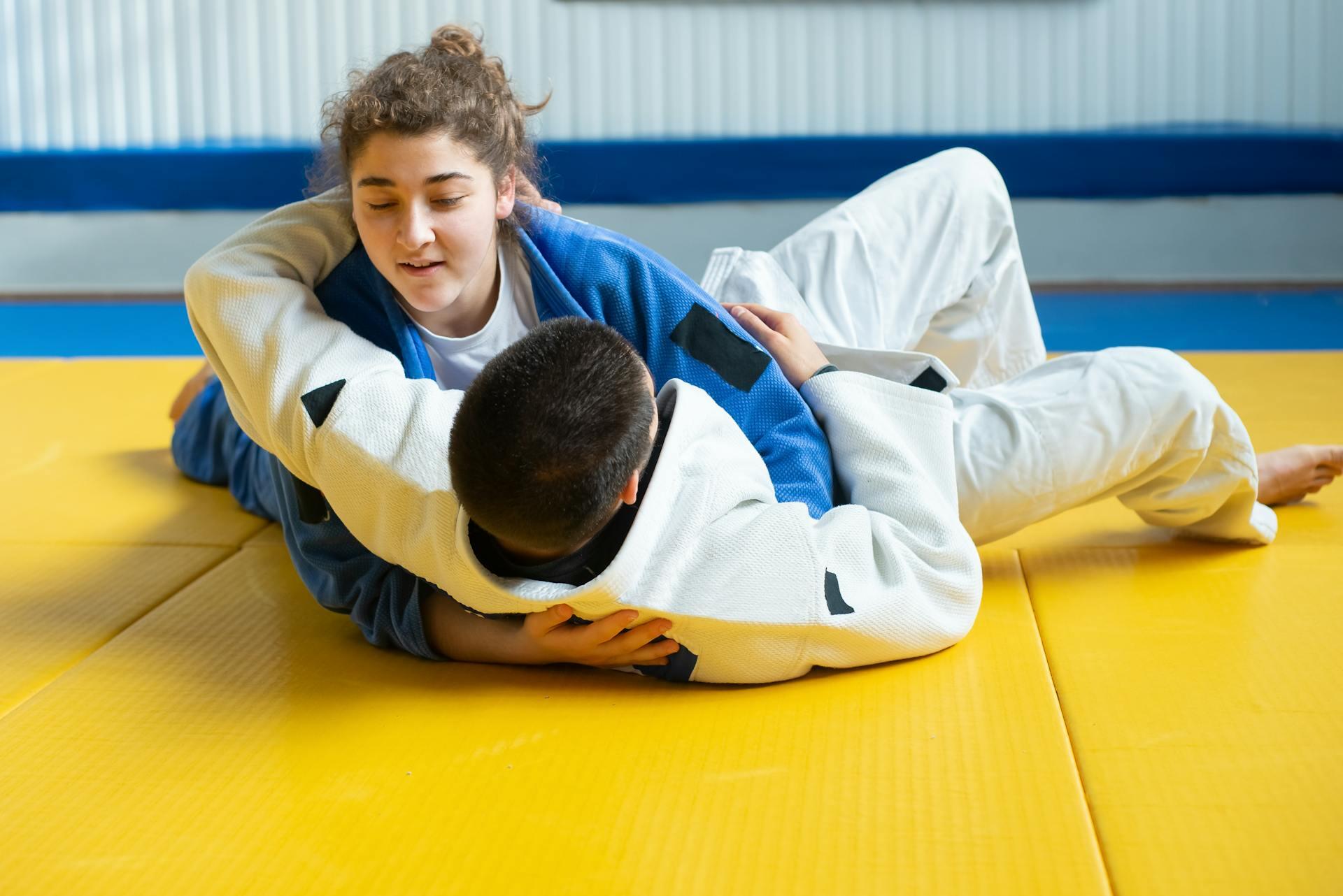 2 teenagers practicing martial arts on a yellow mat.