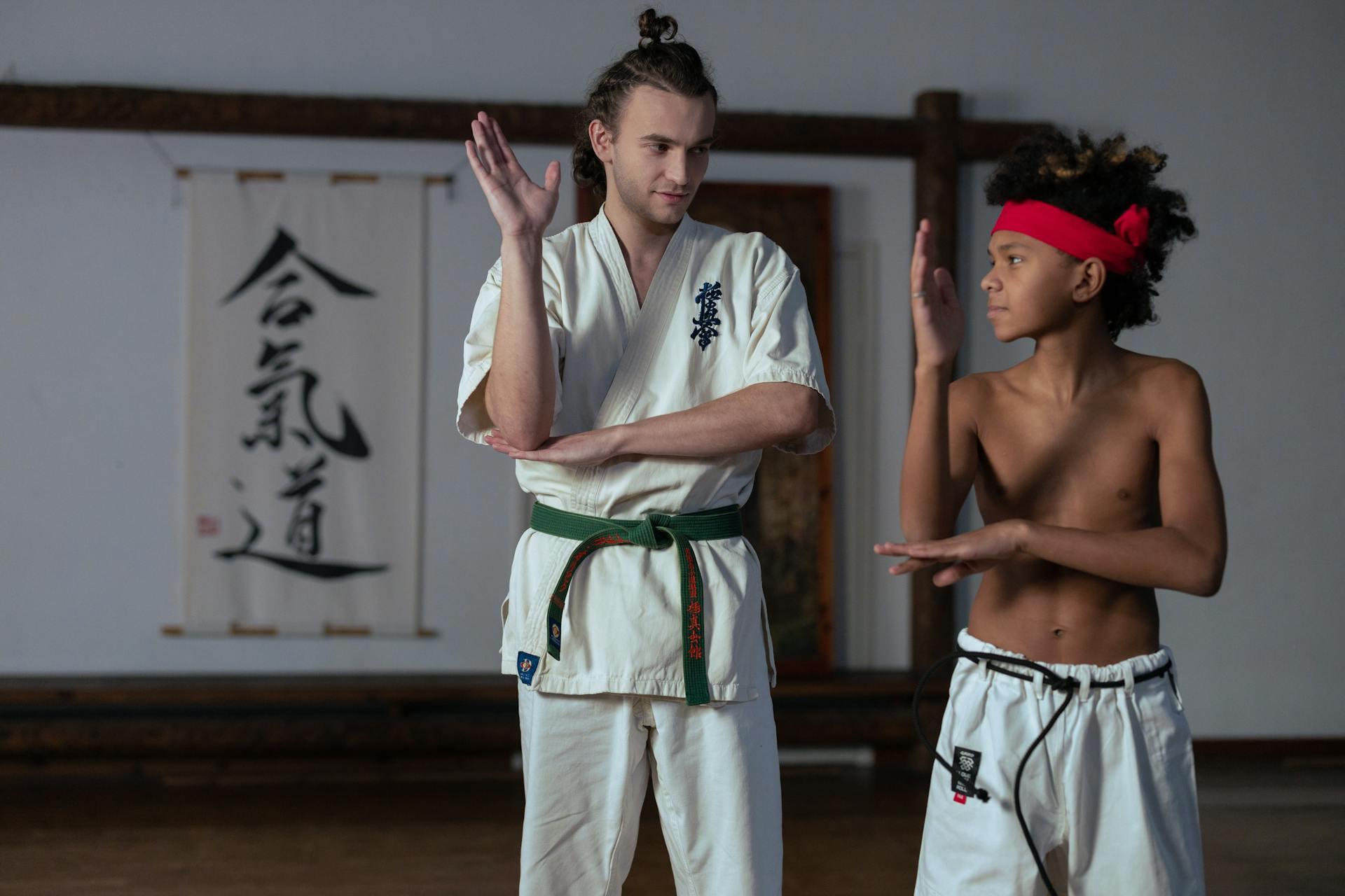 Trainer and boy practicing martial arts, both wearing traditional gear.
