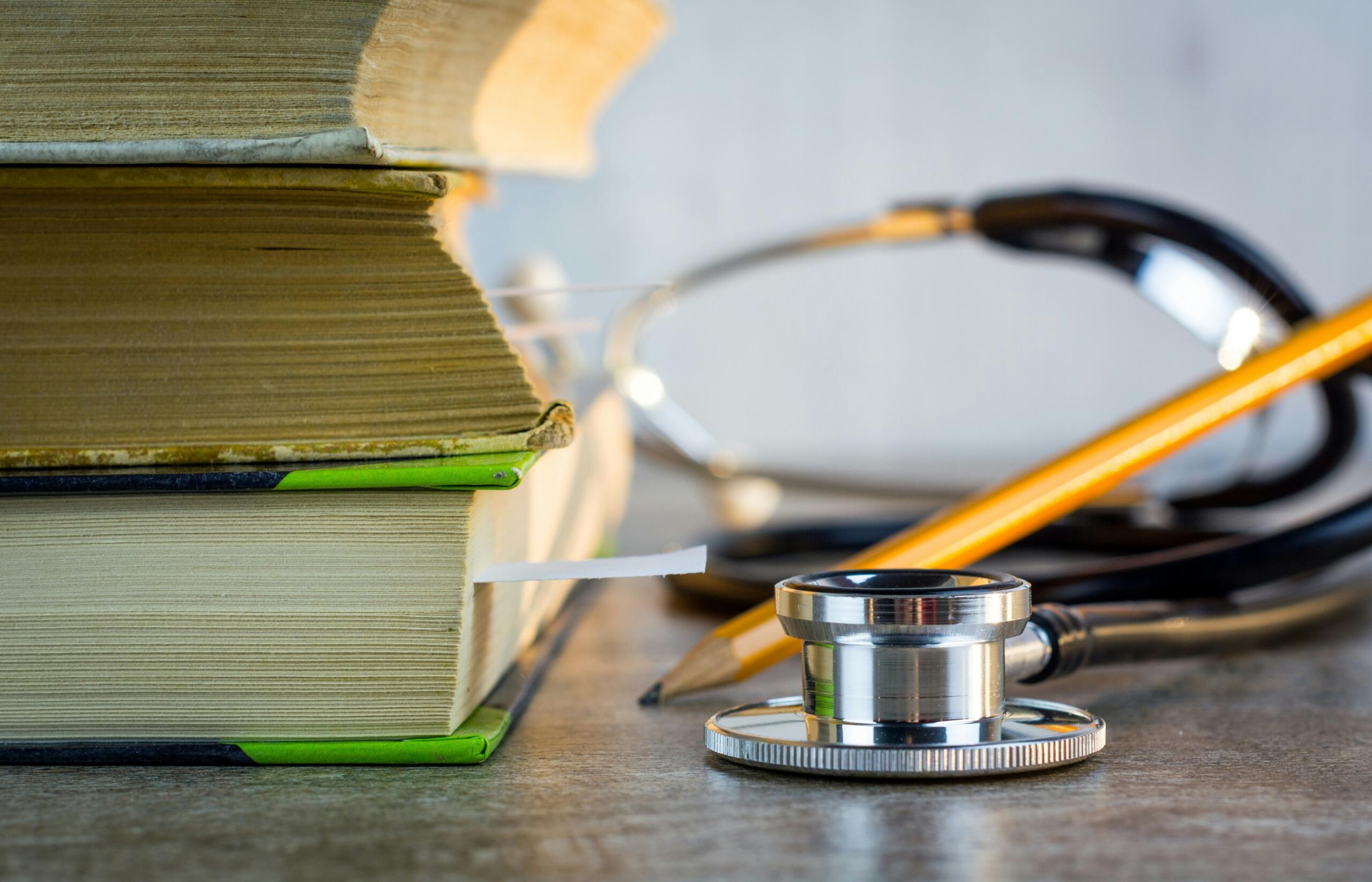 A stack of medical textbooks with a stethoscope and a pencil resting on a table, symbolizing medical studies and education.