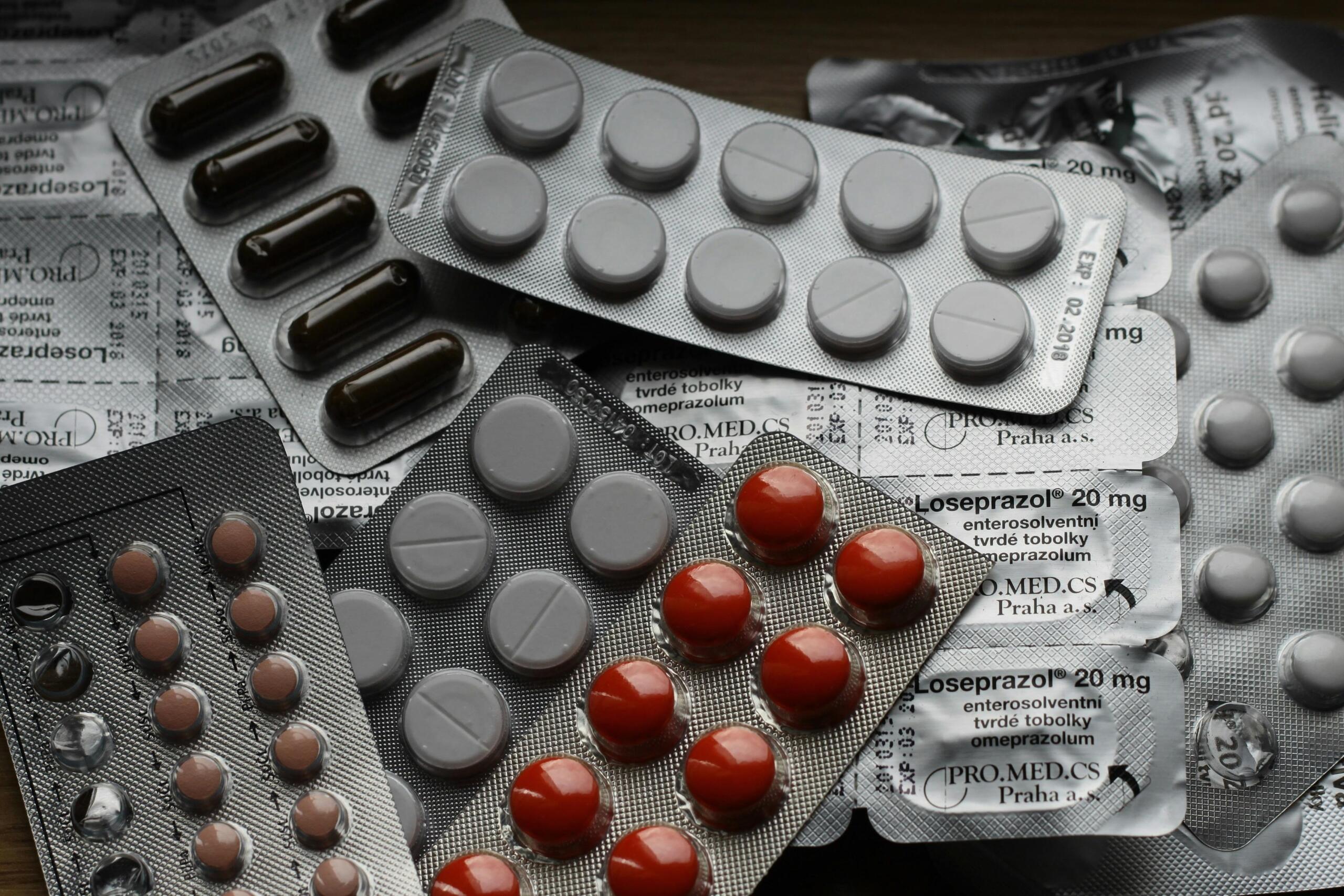 A variety of medical tablets and capsules in blister packs, scattered across a flat surface.