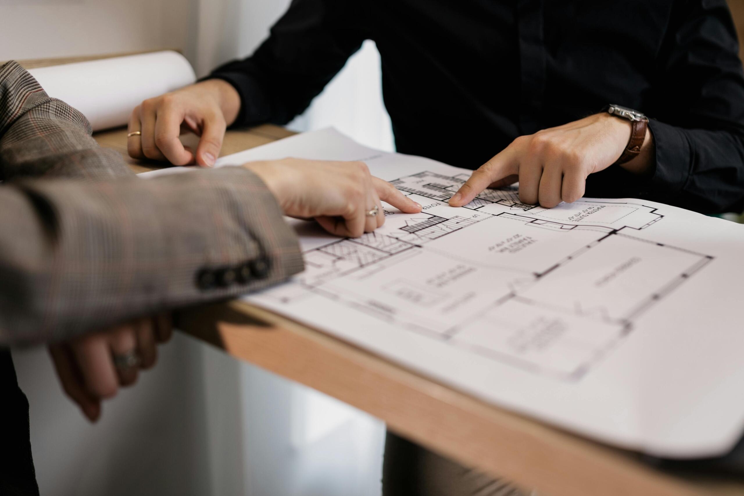 Two people point at different areas of a floor plan for an apartment. Only hands can be seen.