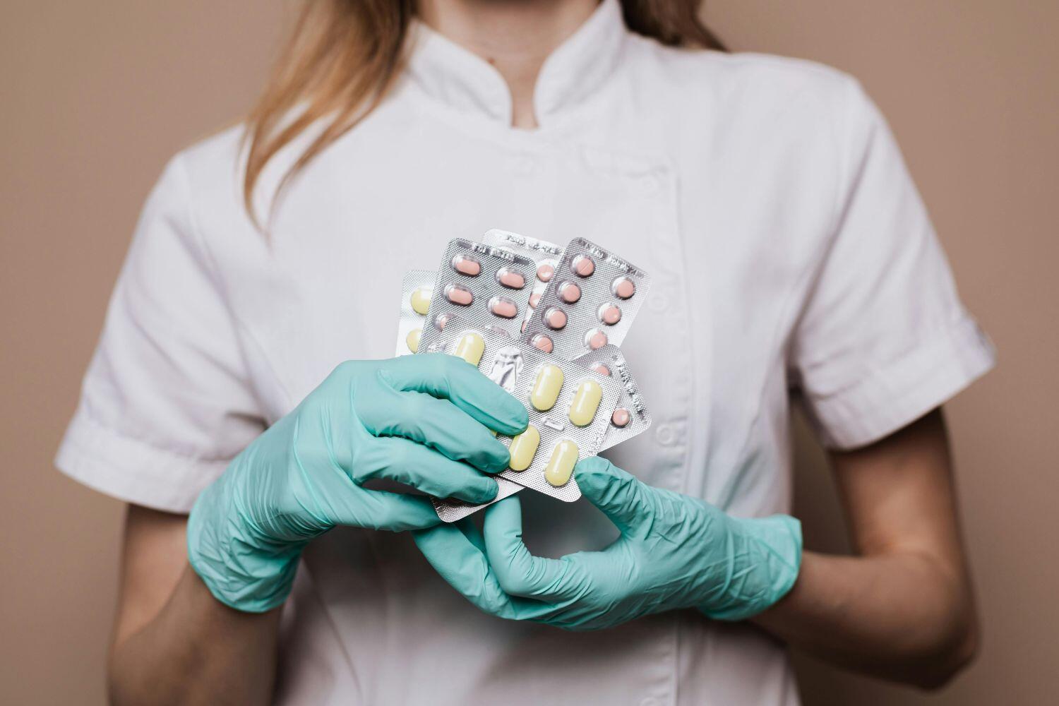 A pharmacist in a white coat holding several blister packs of pills, demonstrating medication management.