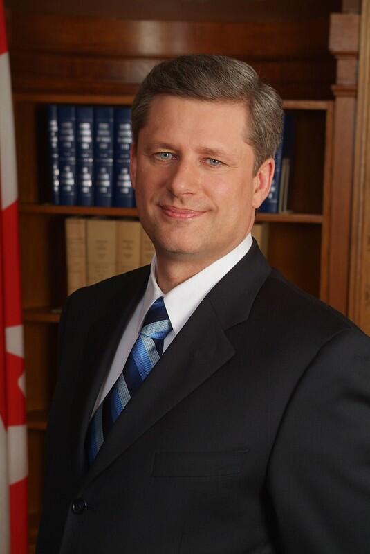 stephen harper posing with a blue tie with a library as backdrop