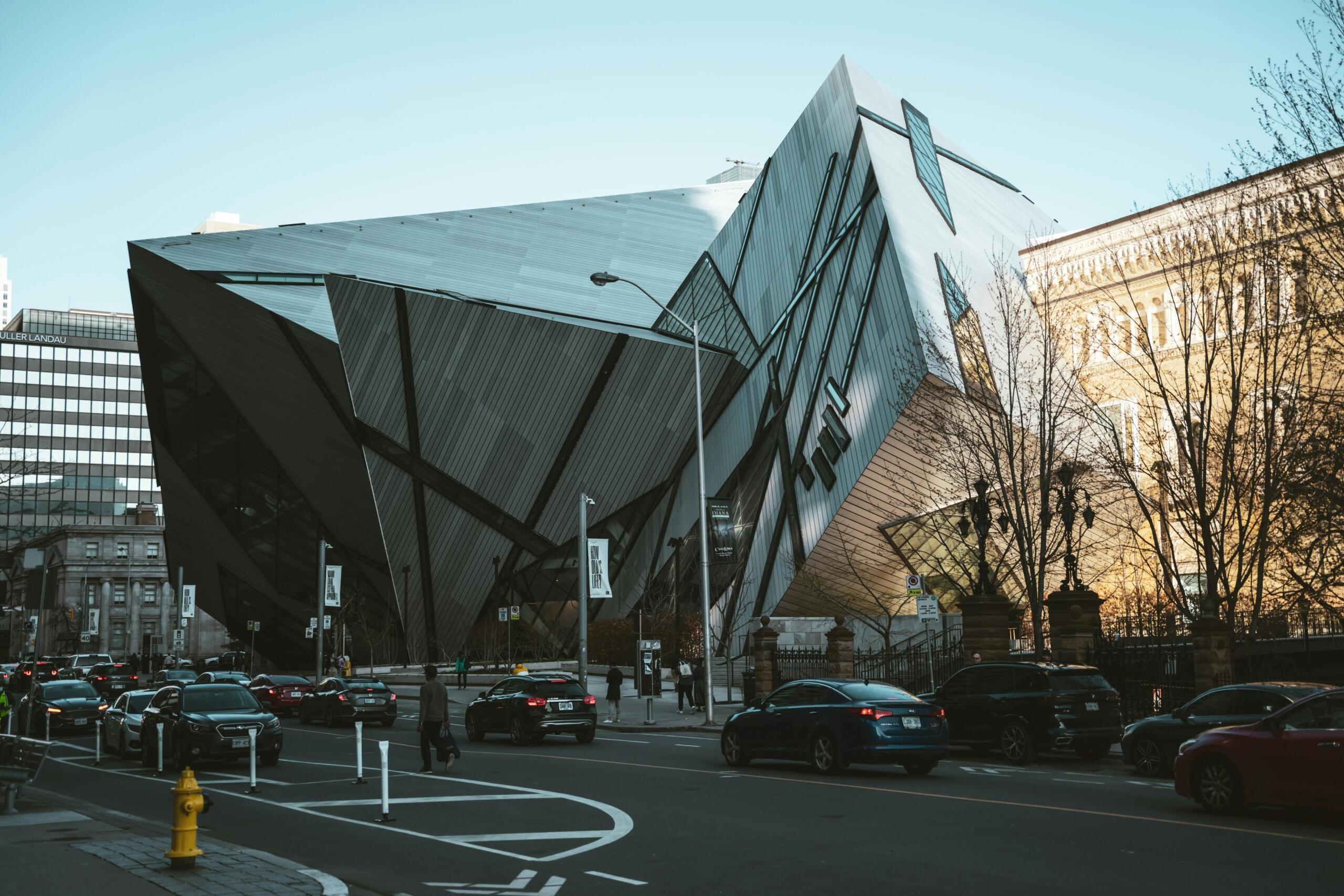 A large structure made of glass stands out in front of a blue sky. The building is the Royal Ontario Museum.
