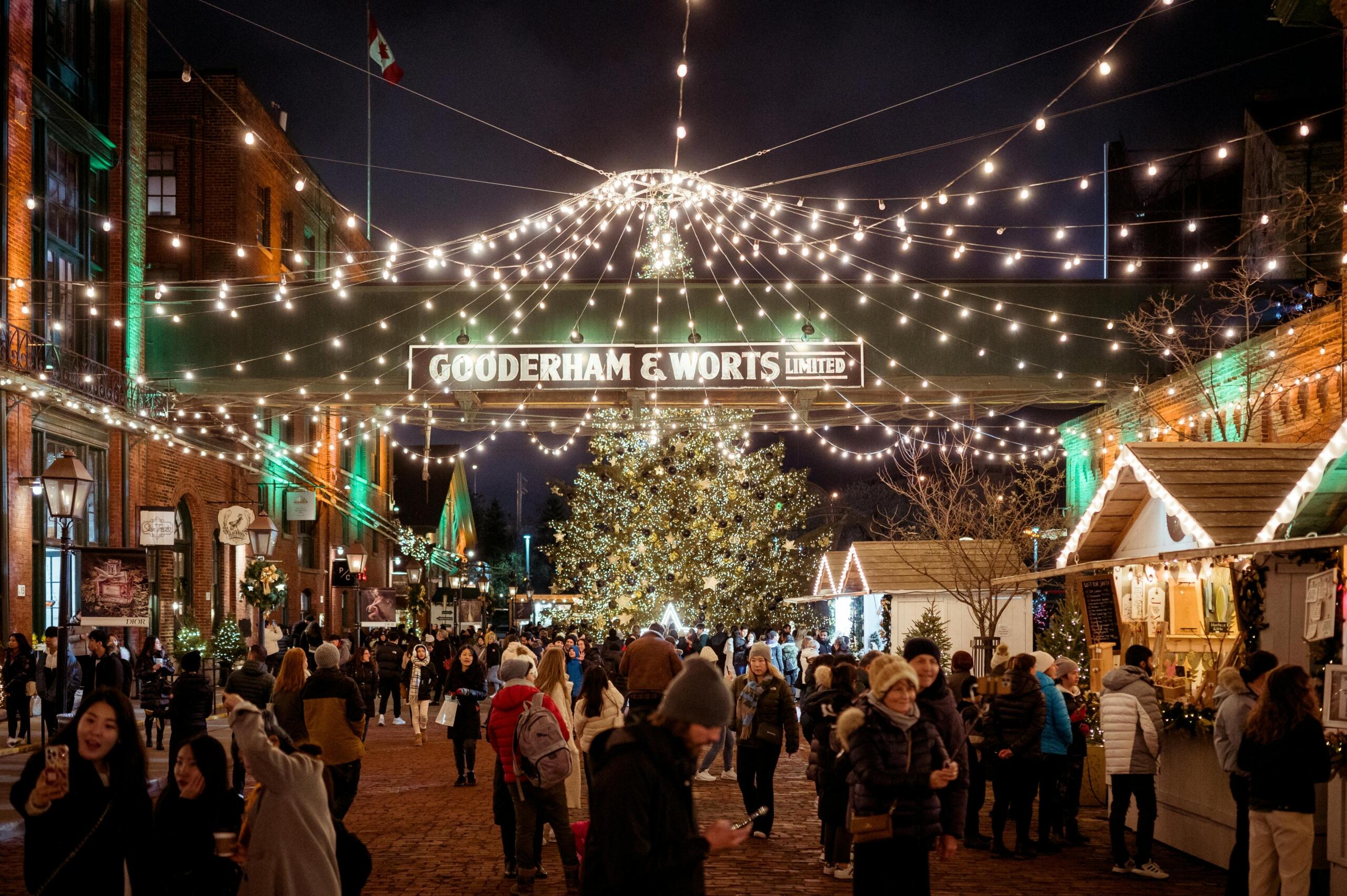 a large christmas tree at night with strings of lights suspended above a holiday market.