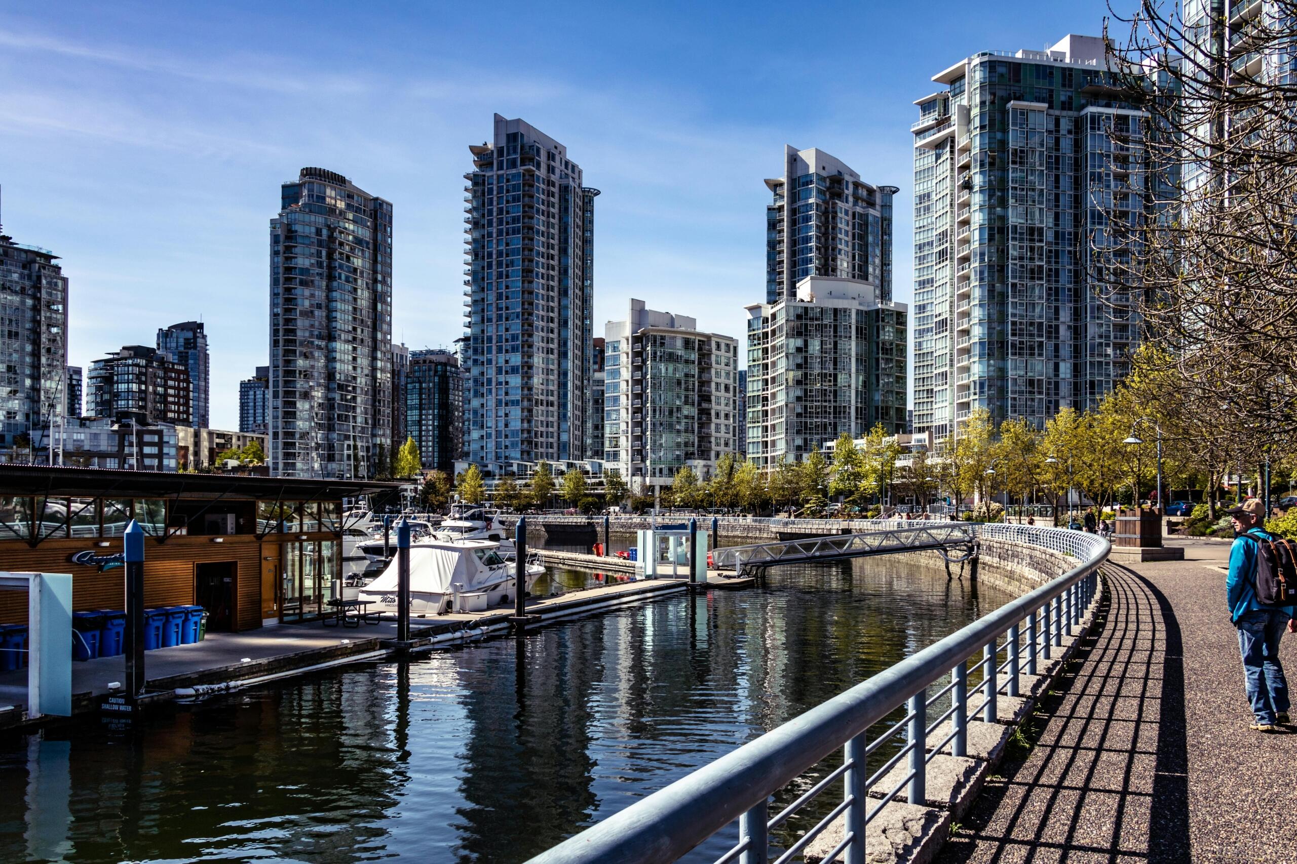 glass condominum buildings on the waterfont of a city. Boats can be seen. A pedestrian walkway is at the front.