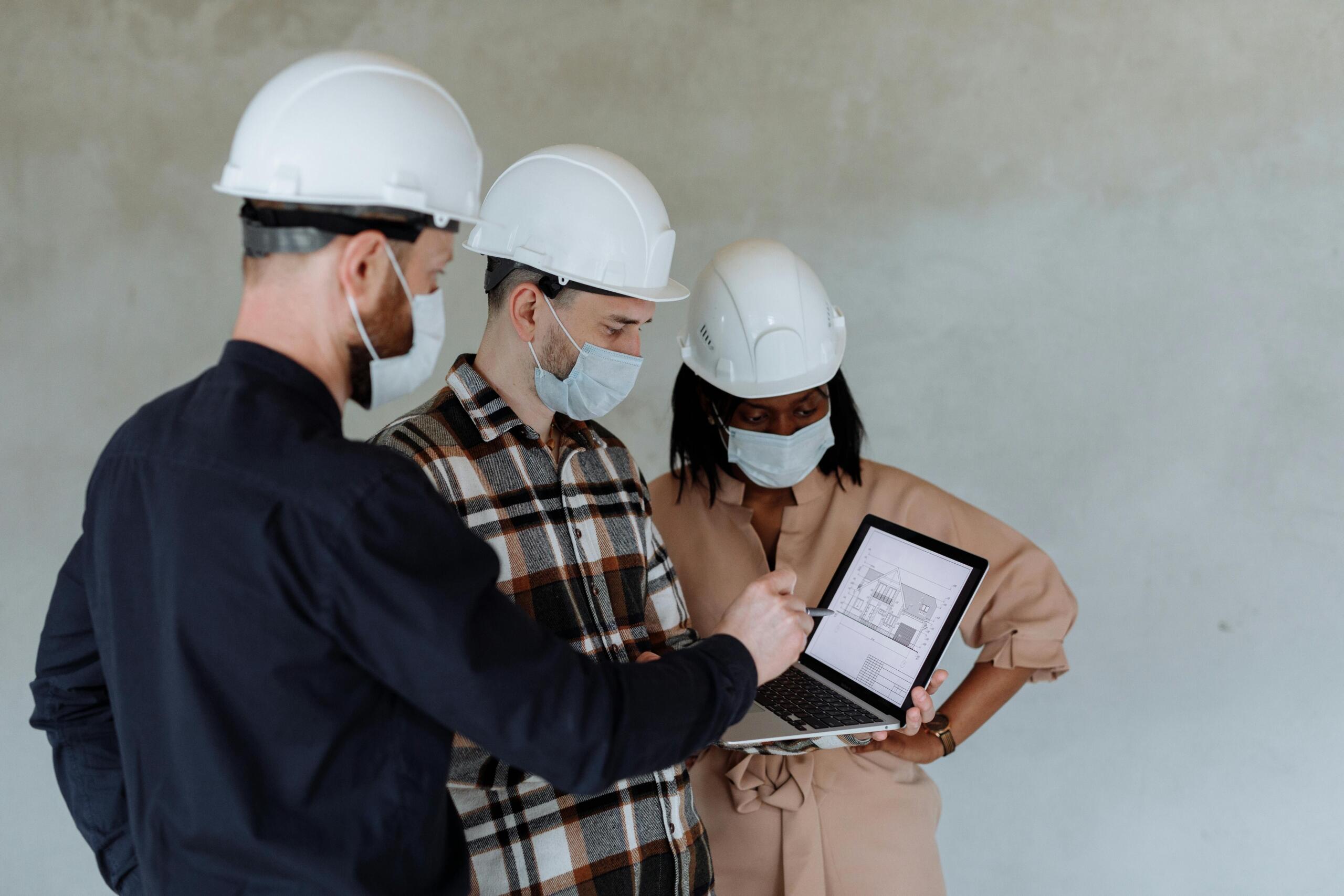 two men and a woman wearing construction hats examine the plan for a house on a computer.