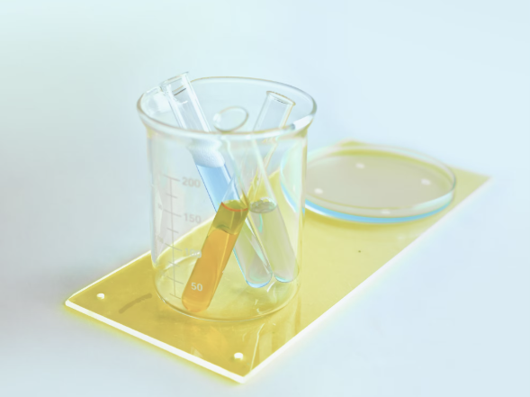 A clear beaker with test tubes containing blue and yellow liquids, placed on a yellow surface next to a petri dish.