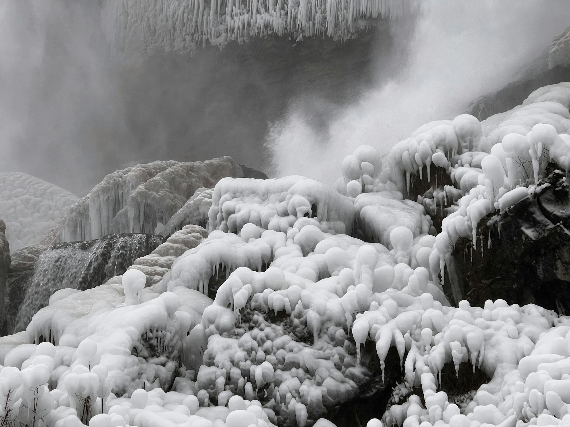 Frozen waterfall with large, dripping ice formations and frosted rocks, enveloped in mist creating a serene, icy landscape.