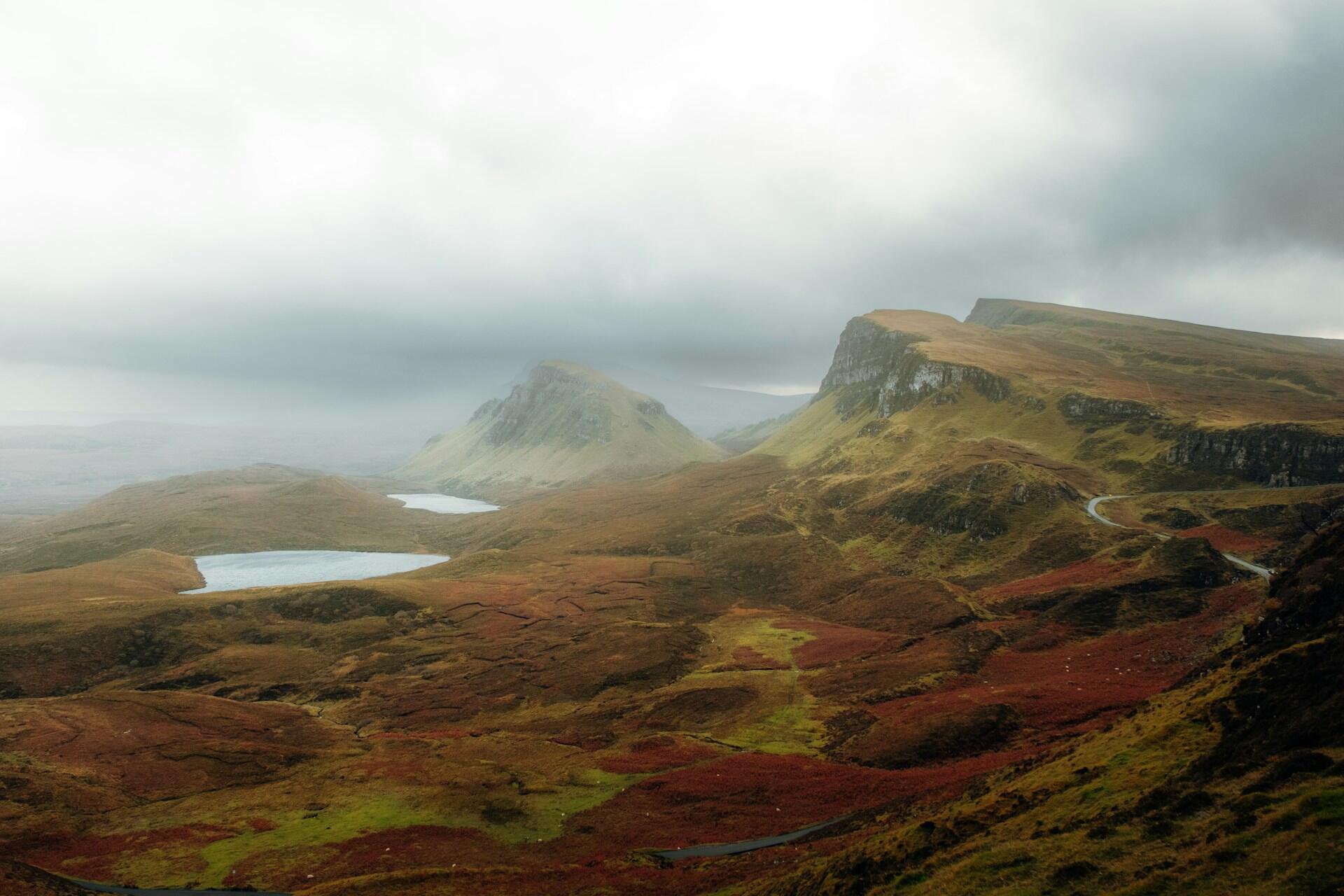 Misty Scottish highlands featuring rolling hills, a winding road, and tranquil lakes surrounded by autumnal hues.