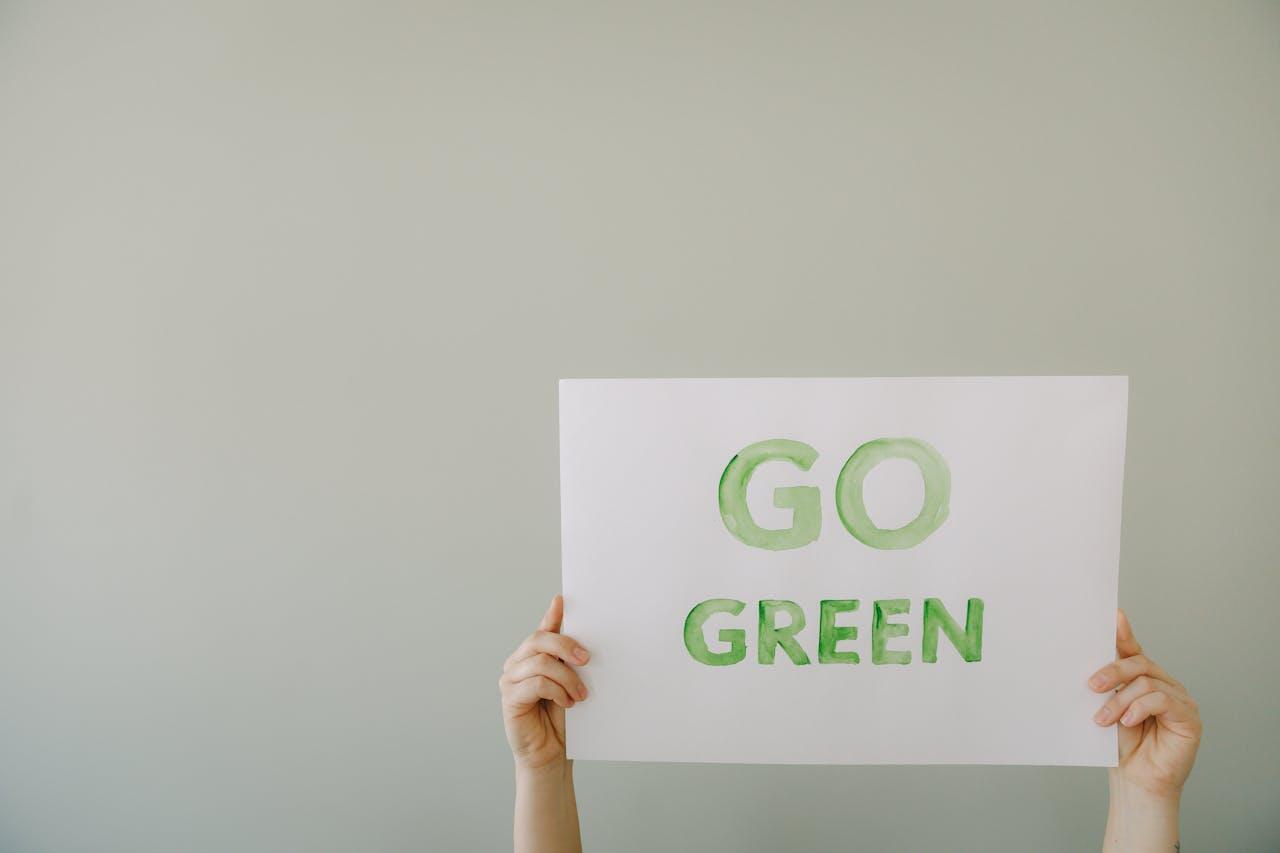 A person holding a white paper with the words go green.